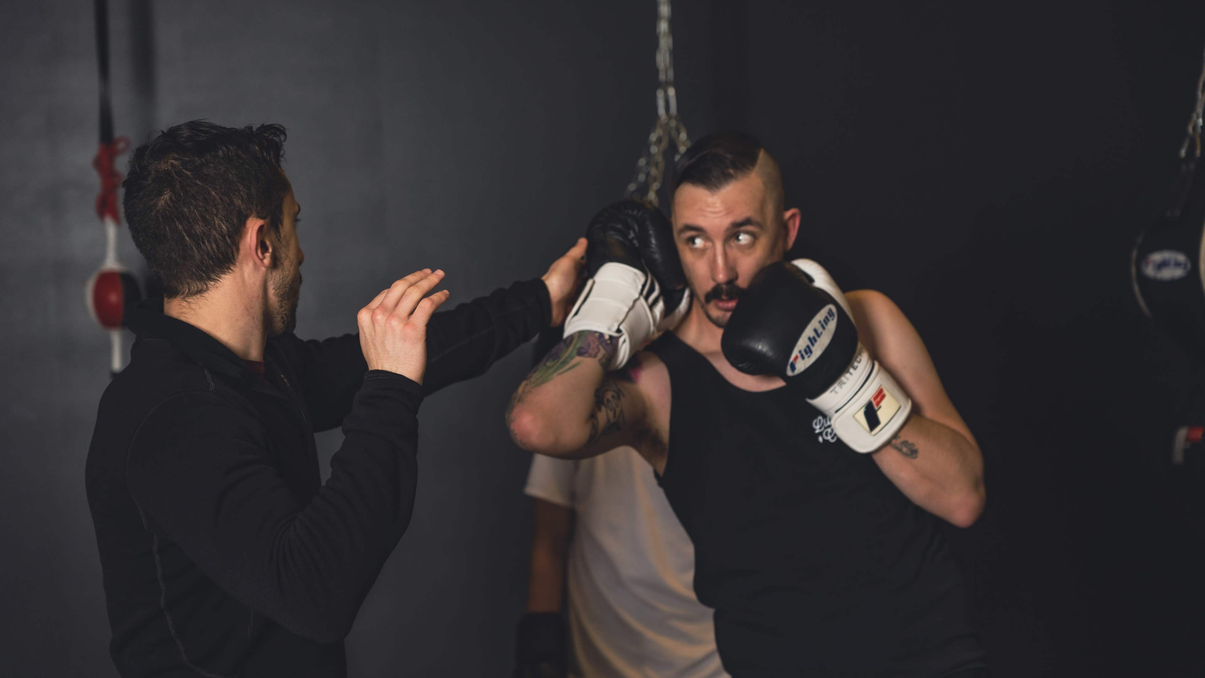 Two men are sparring in a boxing gym, with one man throwing a punch while the other protects himself with gloves.