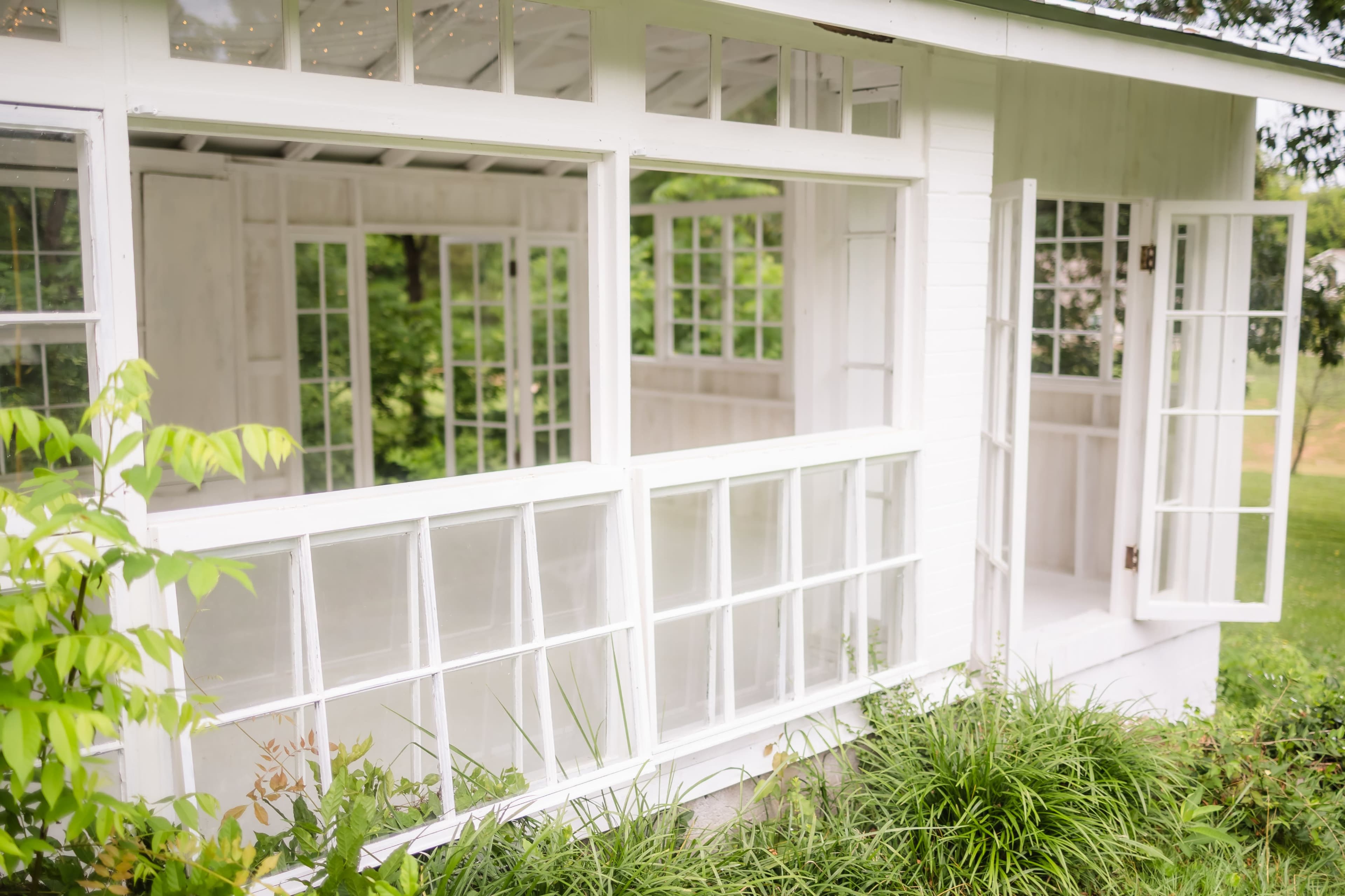 The image shows a white, open-sided structure with multiple windows and doors, surrounded by greenery.