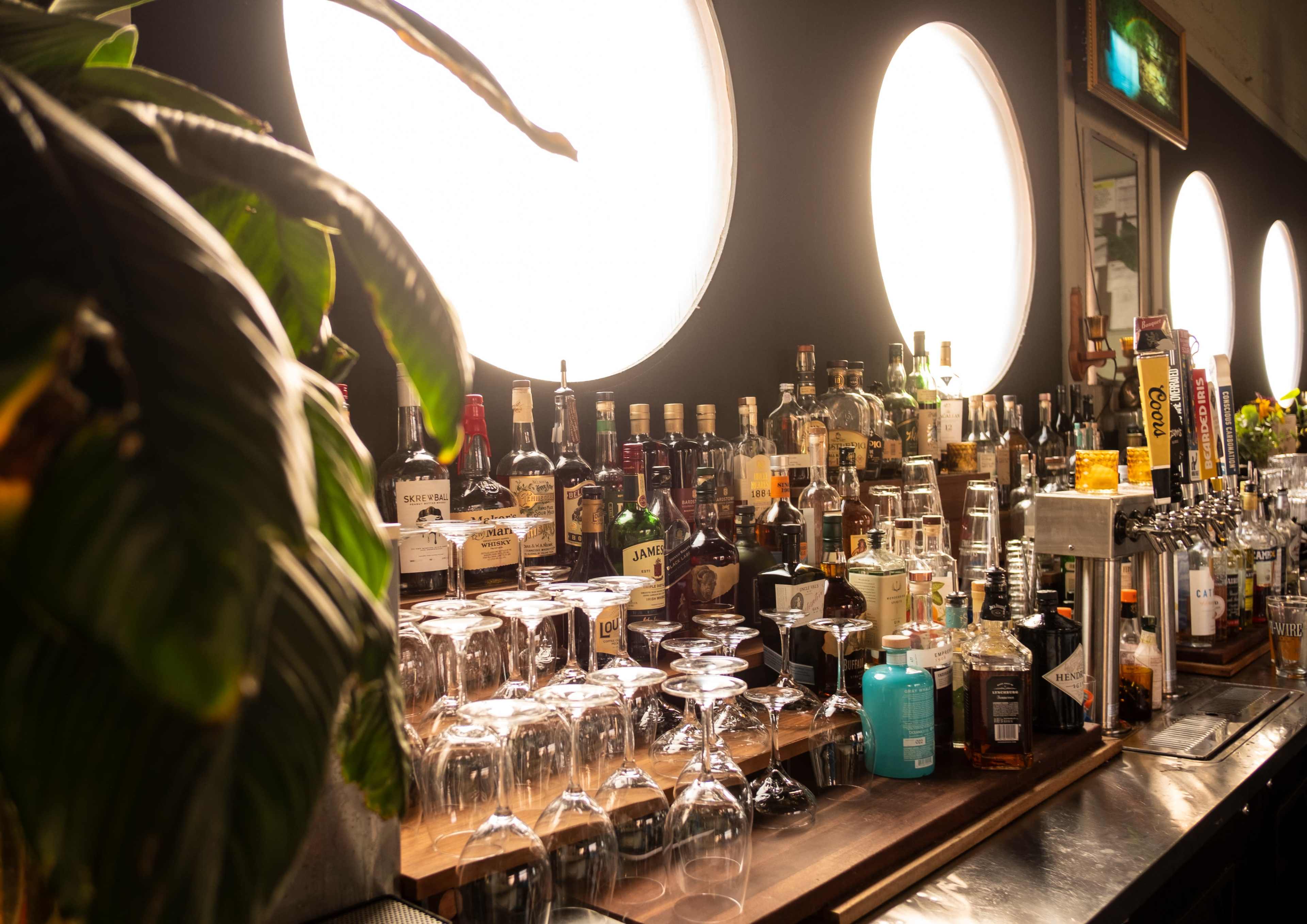 A well-stocked bar displays a variety of liquor bottles and glassware under large circular windows.