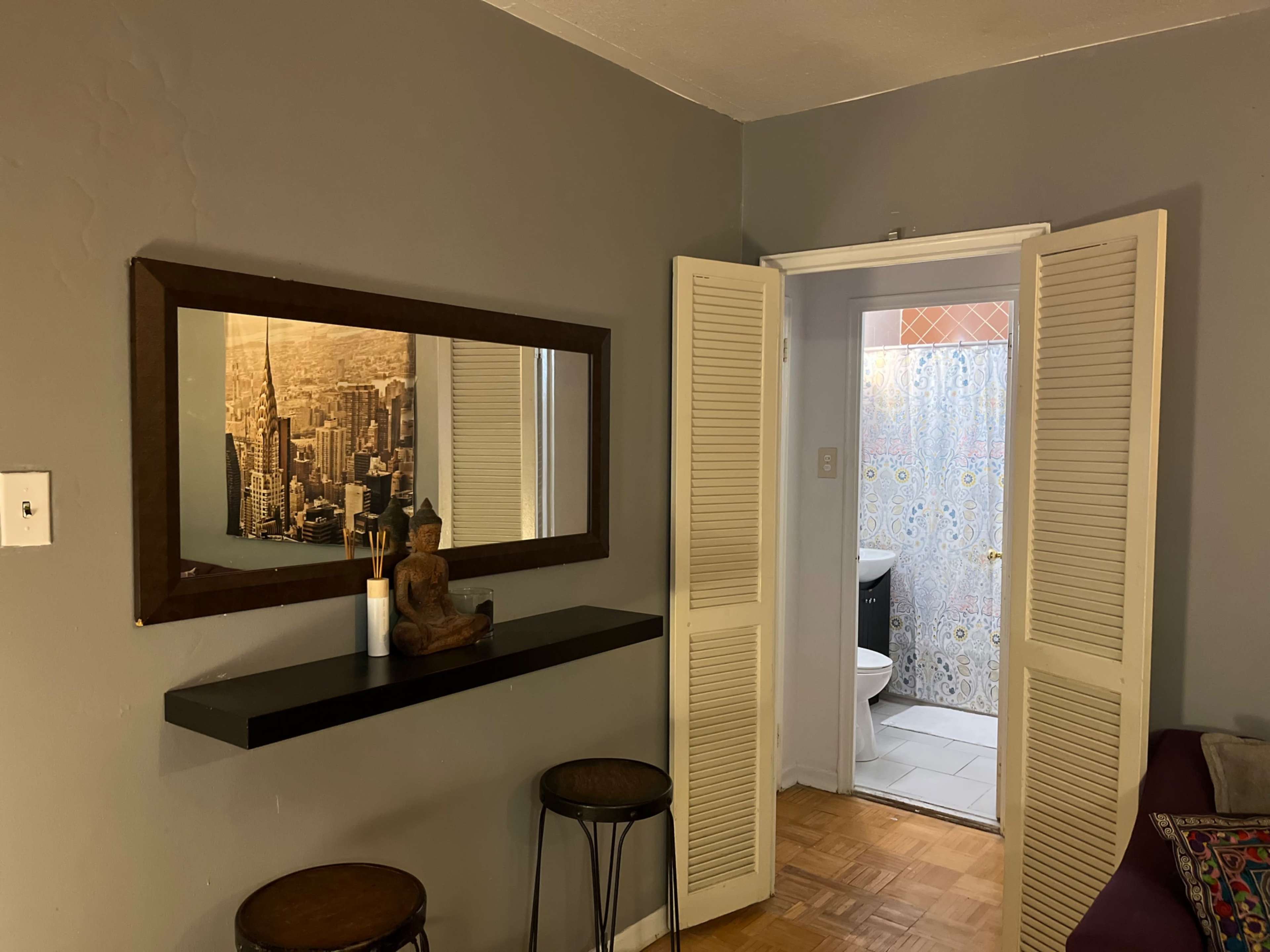 A room with a mirror and a statue on a shelf, leading to a bathroom through double doors with a patterned curtain.