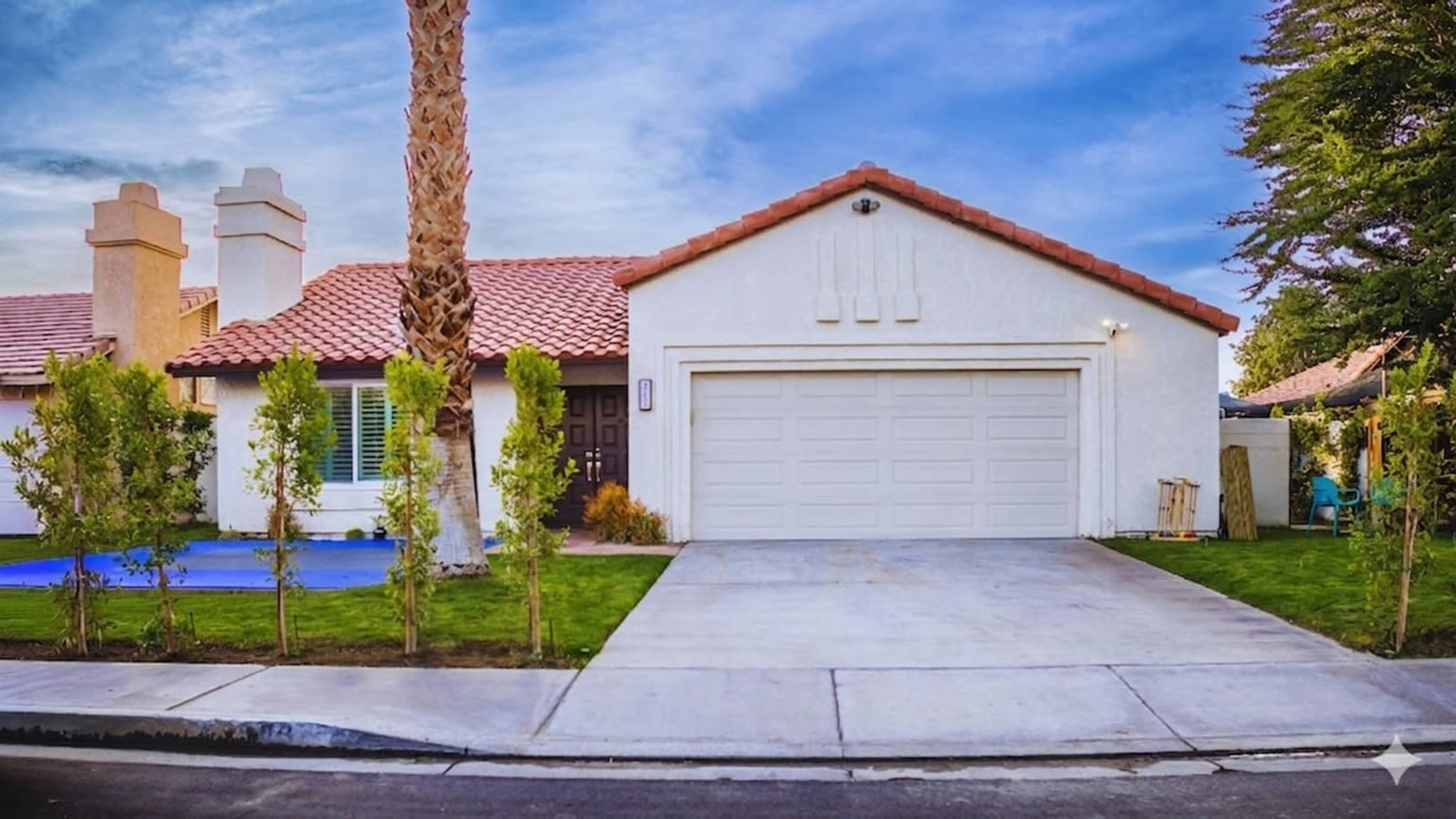 The image shows a single-story house with a red tiled roof, a garage, and landscaped front yard on a residential street.