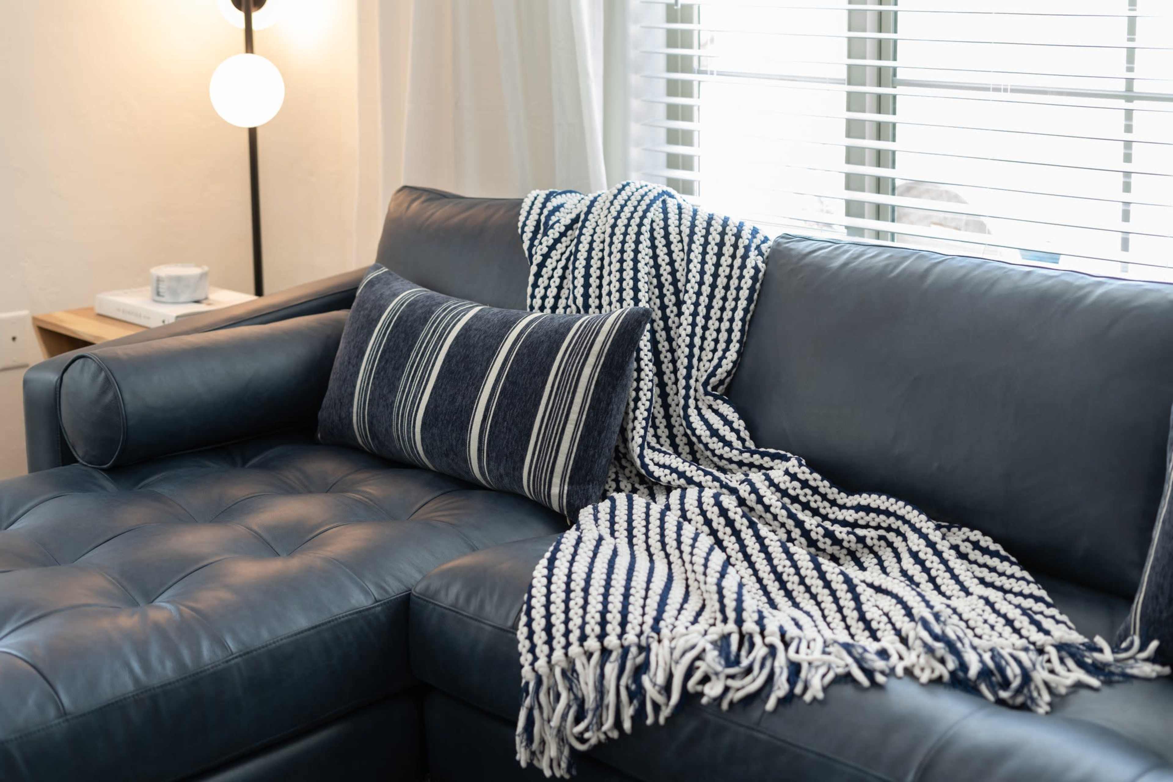 A navy blue leather sectional sofa is adorned with a striped throw pillow and a fringed blanket.