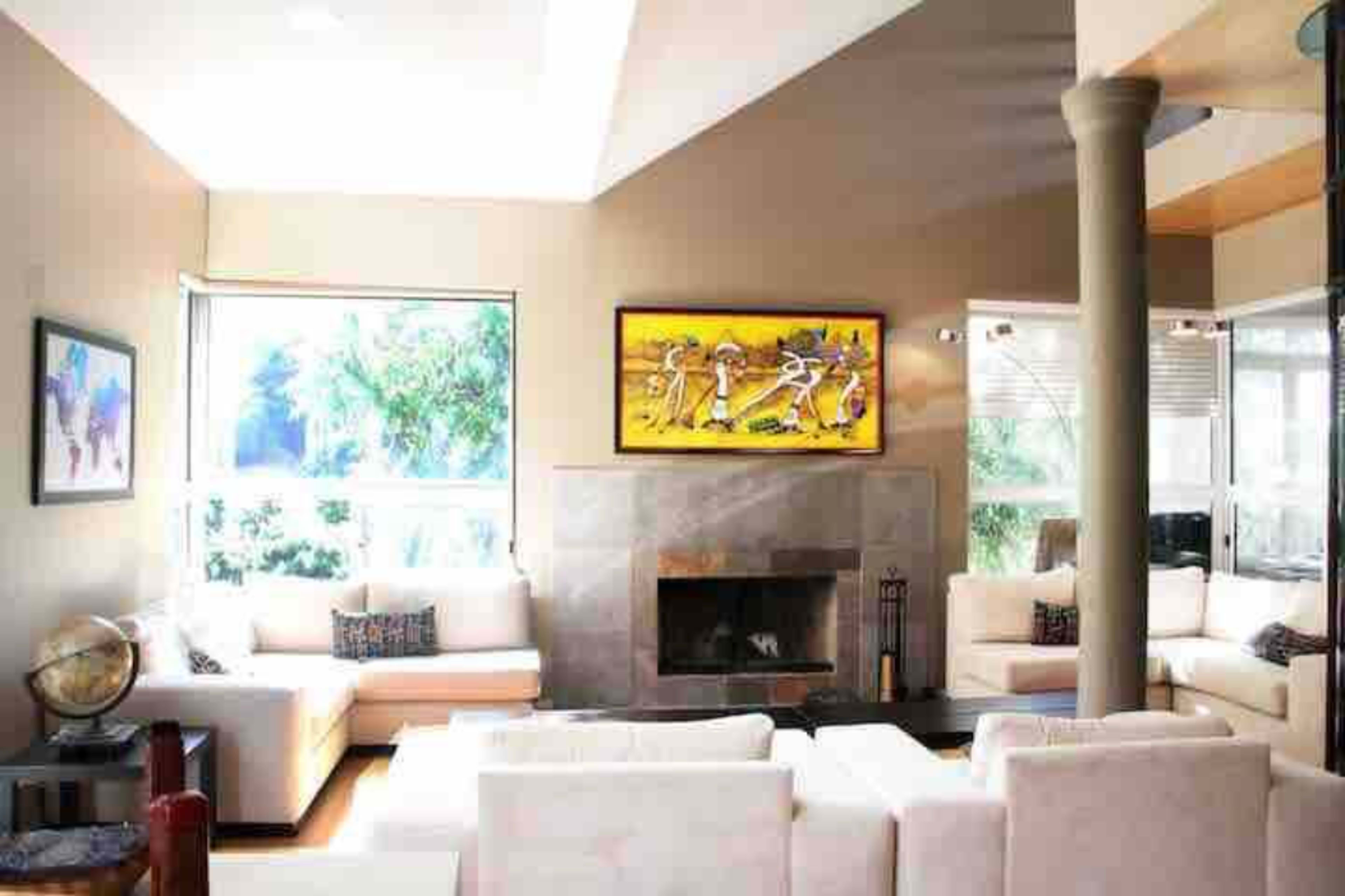 A contemporary living room with a stone fireplace, large windows, and modern white sofas arranged around a coffee table.