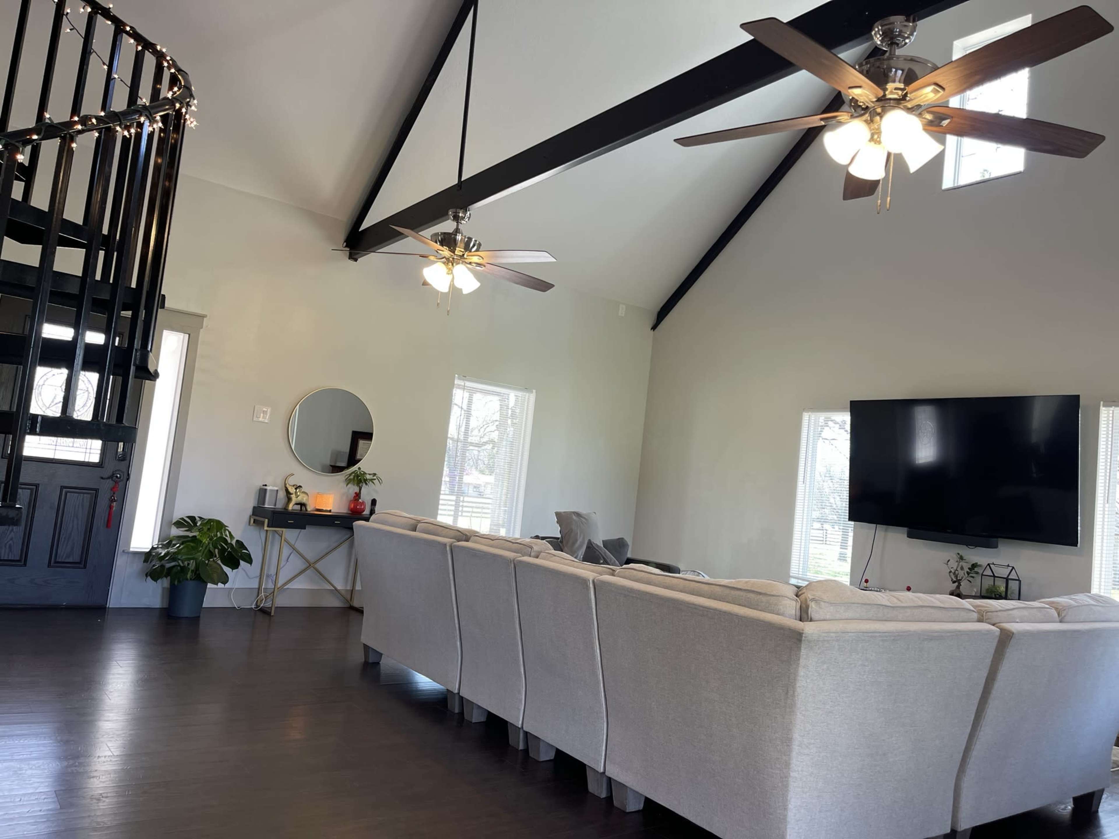 A spacious living room features a sectional sofa, a large wall-mounted television, and ceiling fans, with a spiral staircase in the corner.