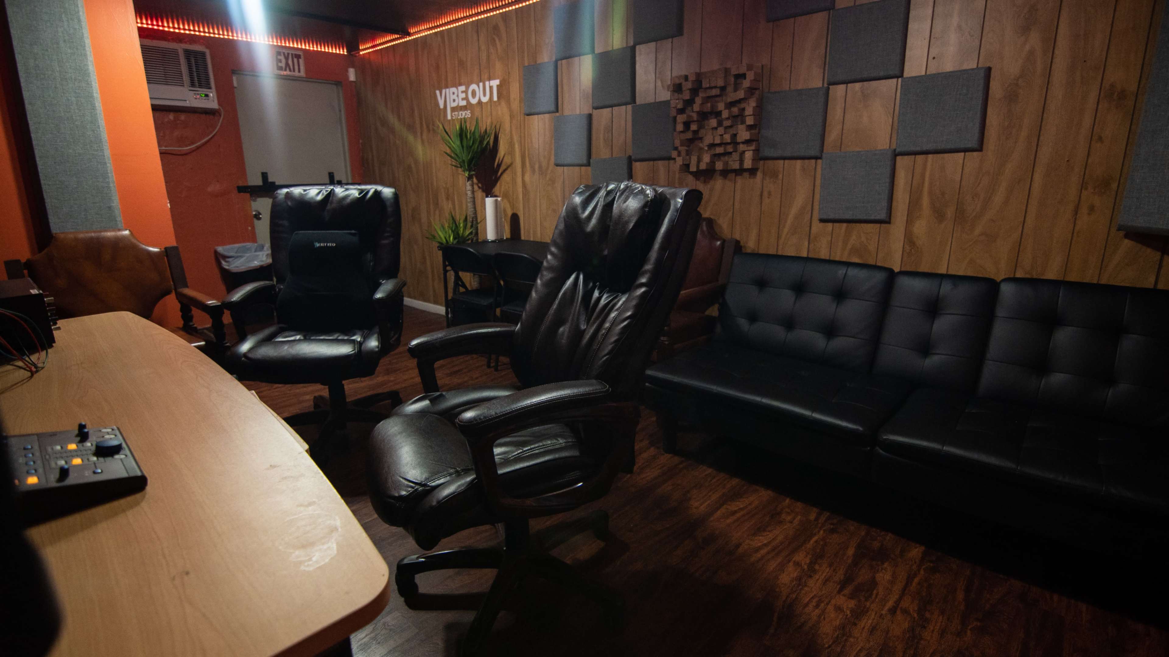 The image shows a recording studio with leather chairs, a couch, and soundproofing panels on the wooden walls.