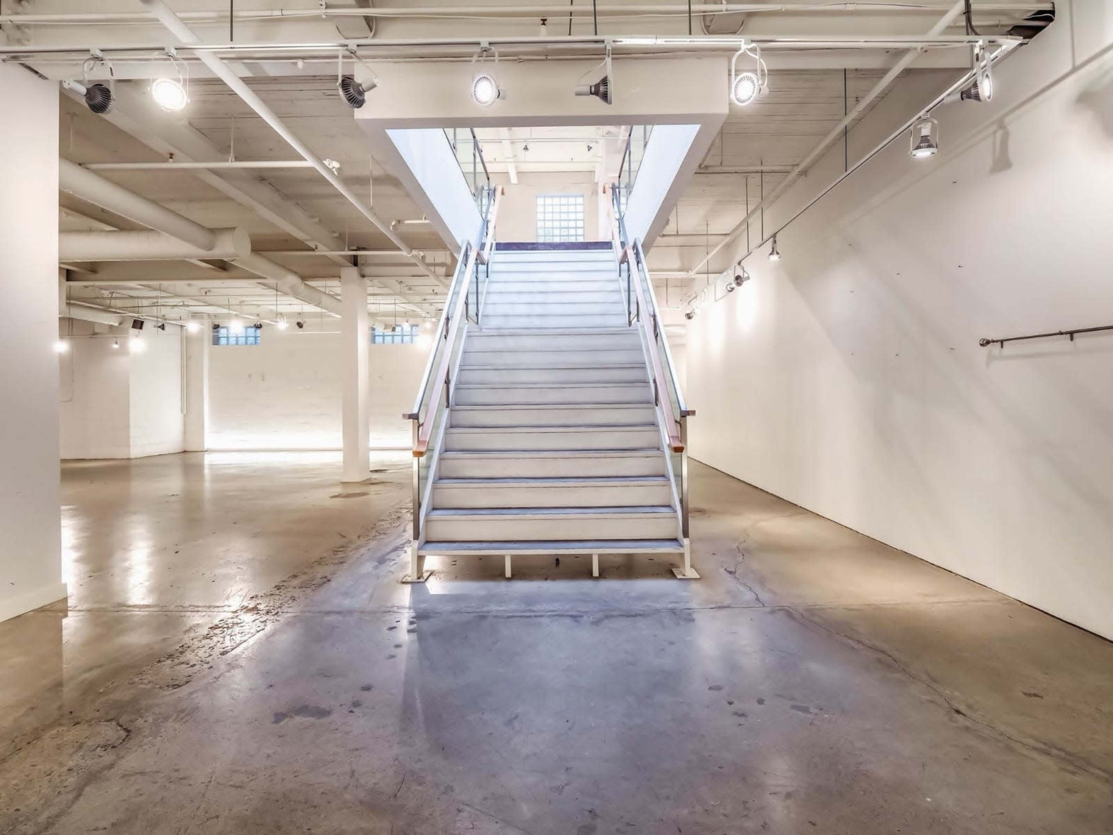 A spacious, well-lit gallery with a central staircase leading to an upper level.