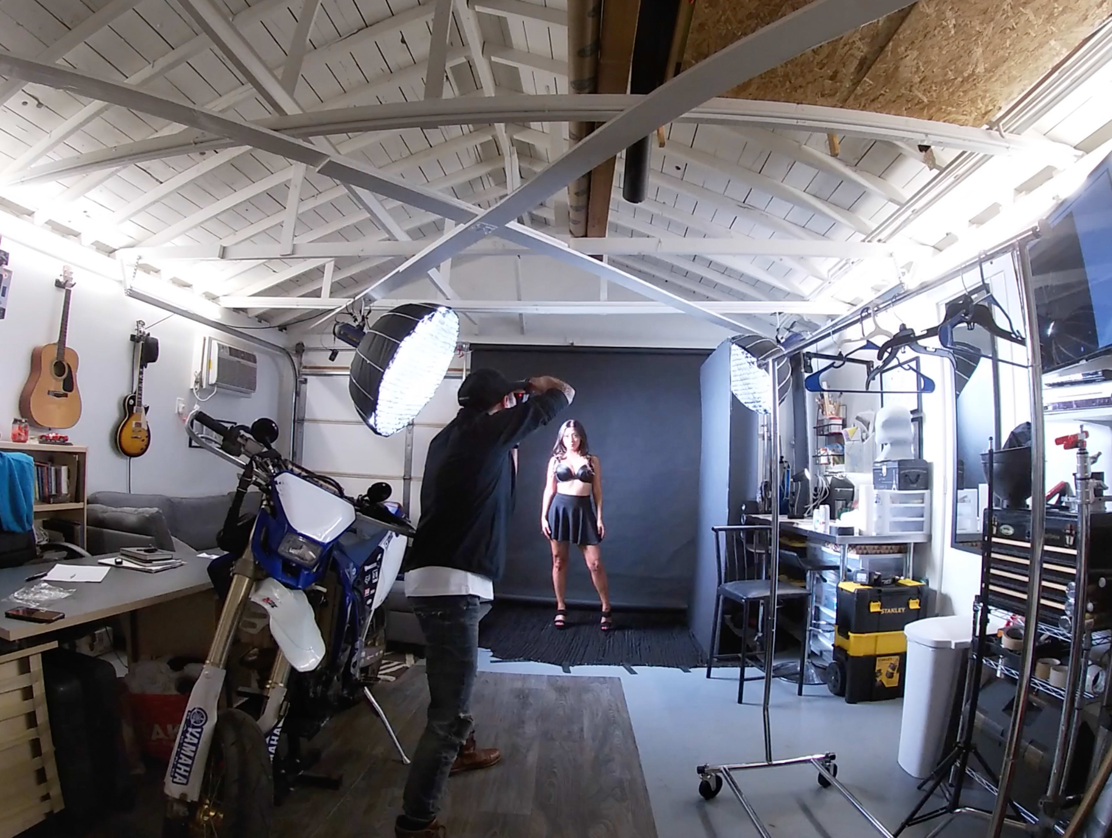 A photographer is taking a picture of a model wearing a black dress in a studio setting with multiple lighting setups.
