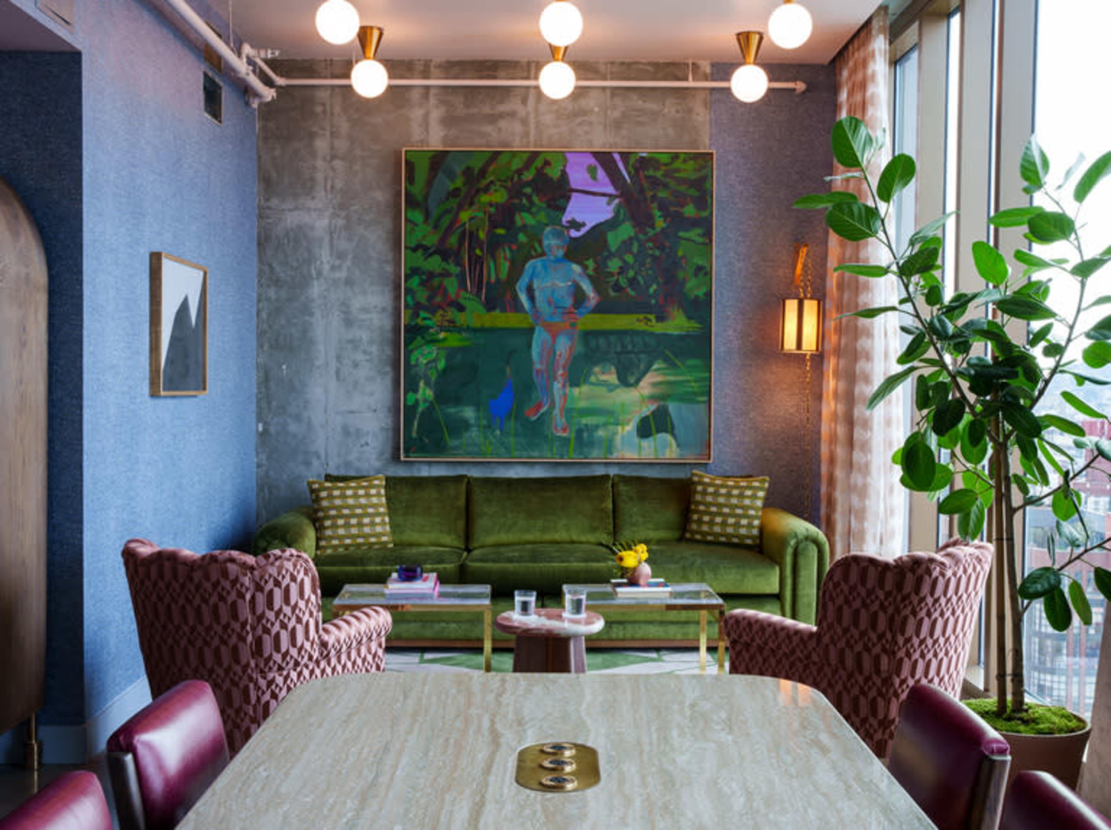 A modern living space features a green sofa, two patterned chairs, a large artwork on the wall, and a potted plant, with natural light coming through large windows.