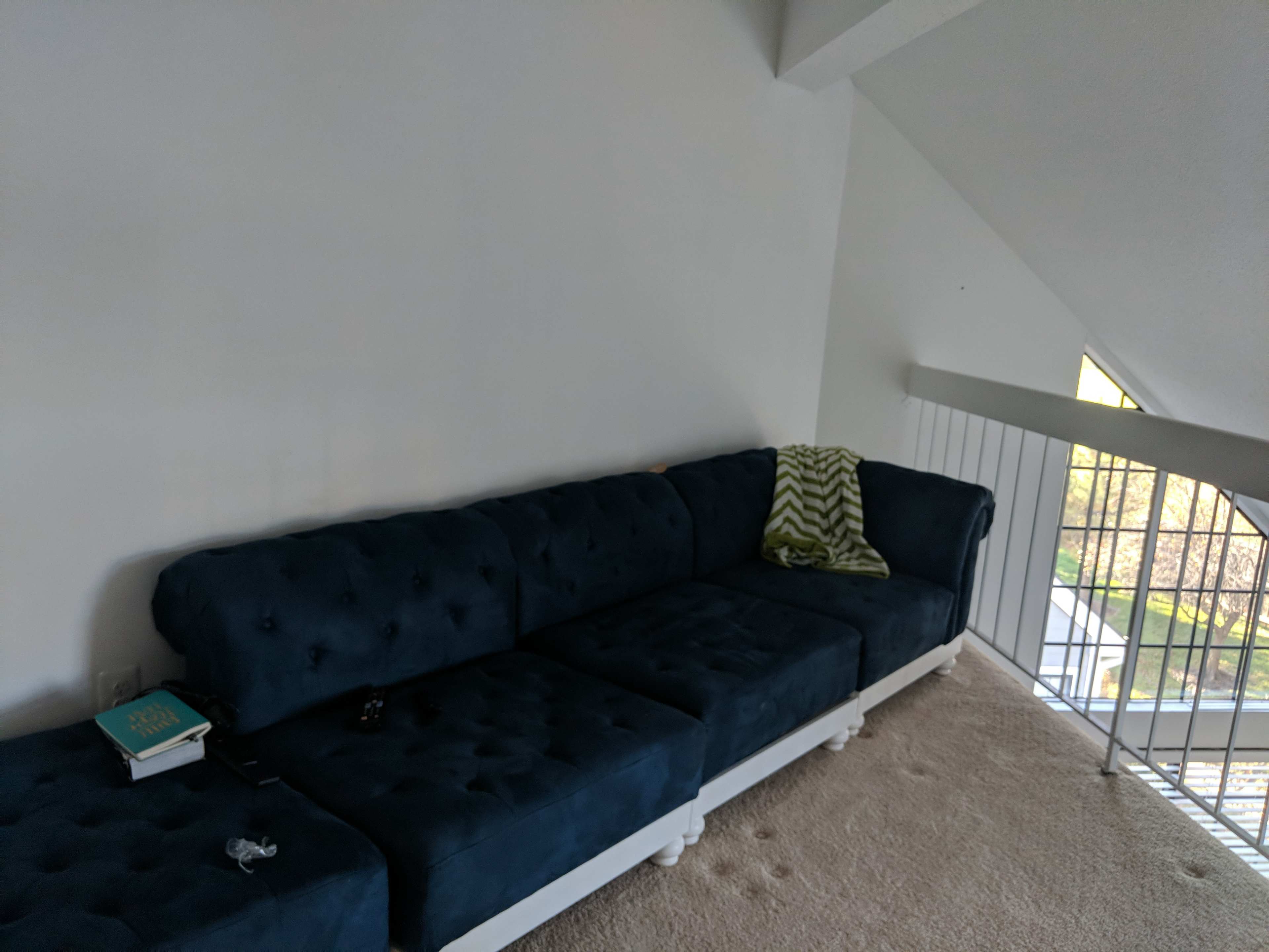 A blue tufted sectional couch sits against a white wall in a well-lit room with a sloped ceiling.