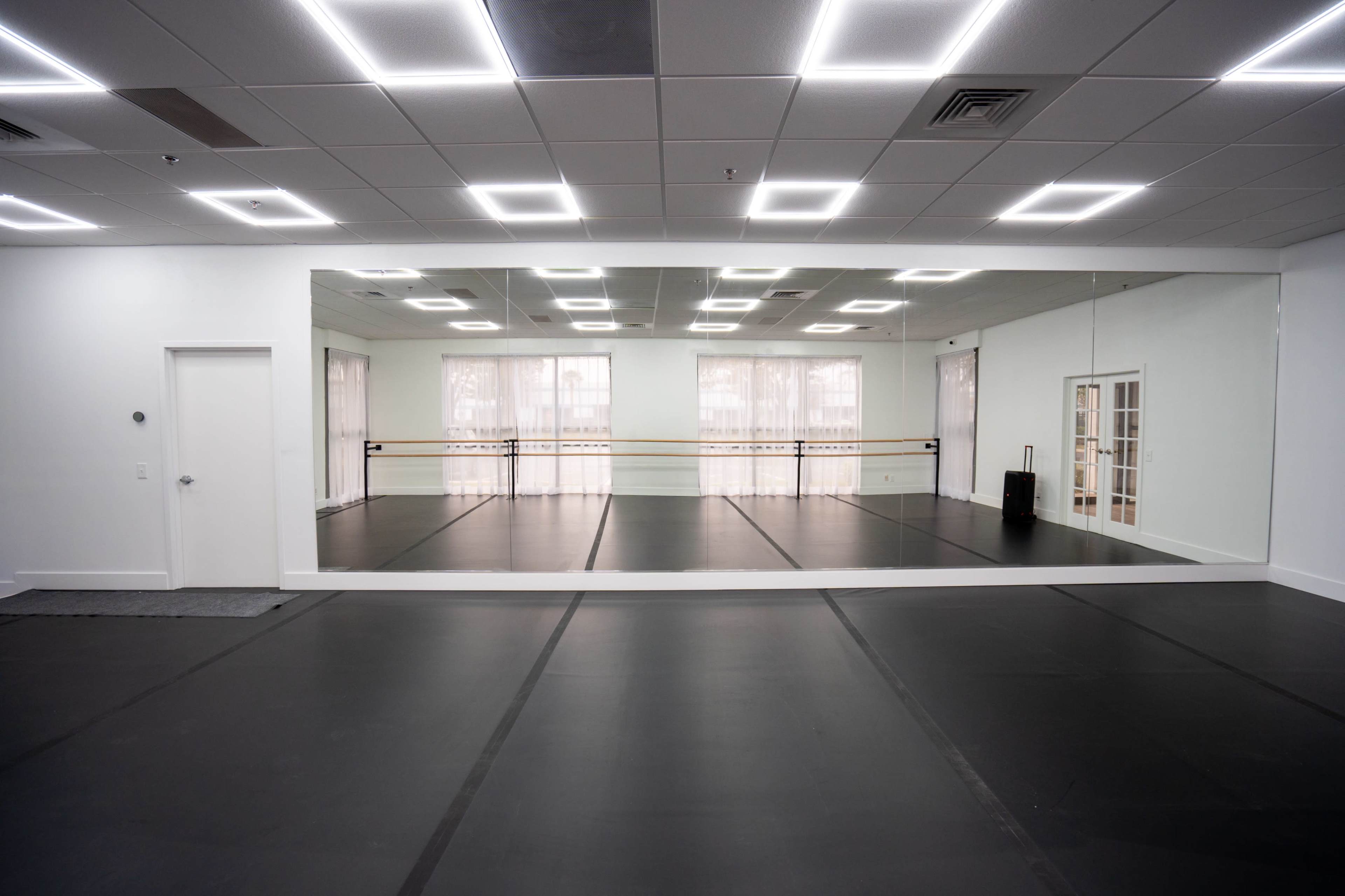 The image shows a spacious, mirrored dance studio with a dark floor and bright overhead lights.