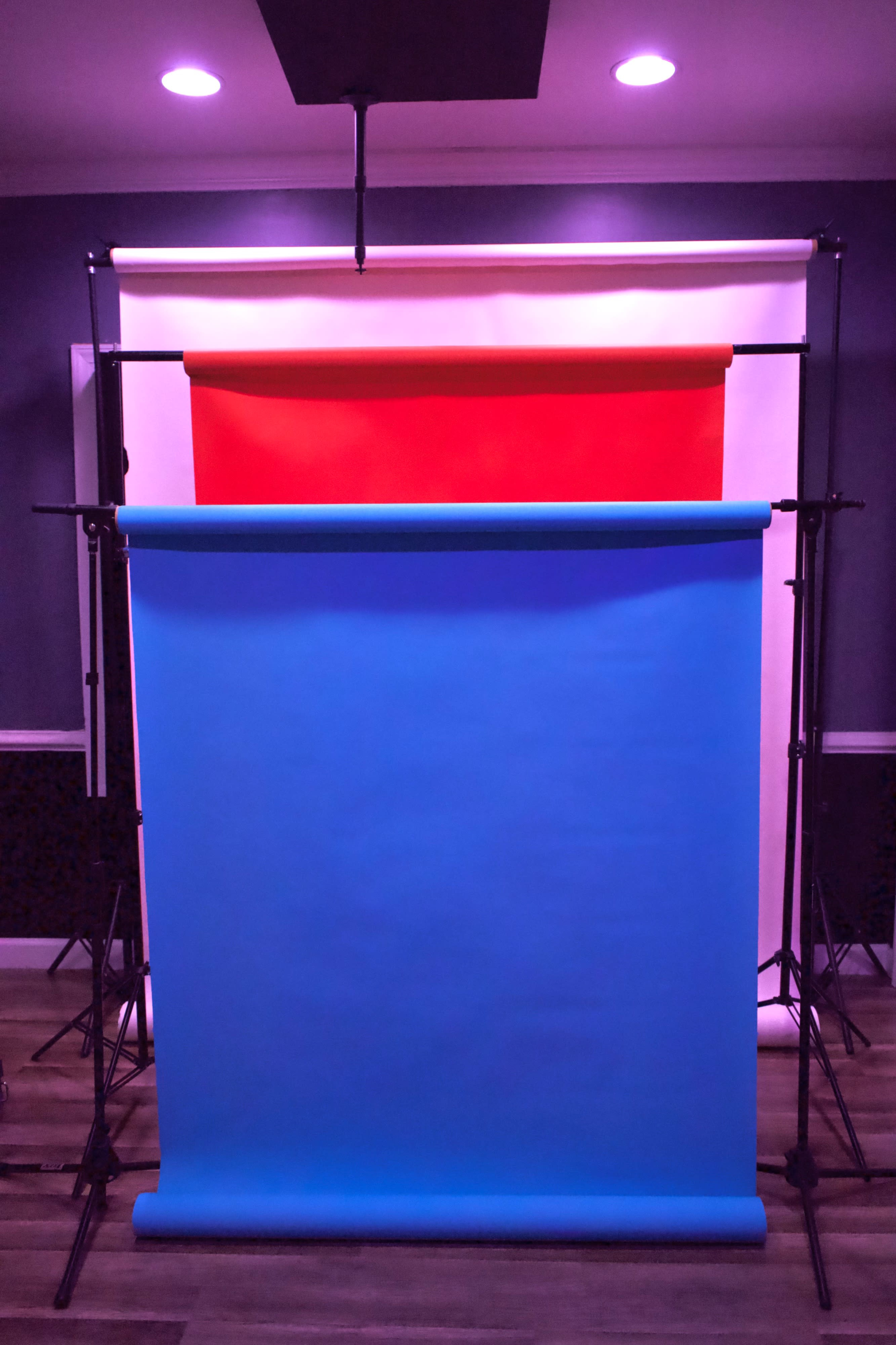 Three backdrop paper rolls in red, white, and blue, mounted on stands in a studio setting.
