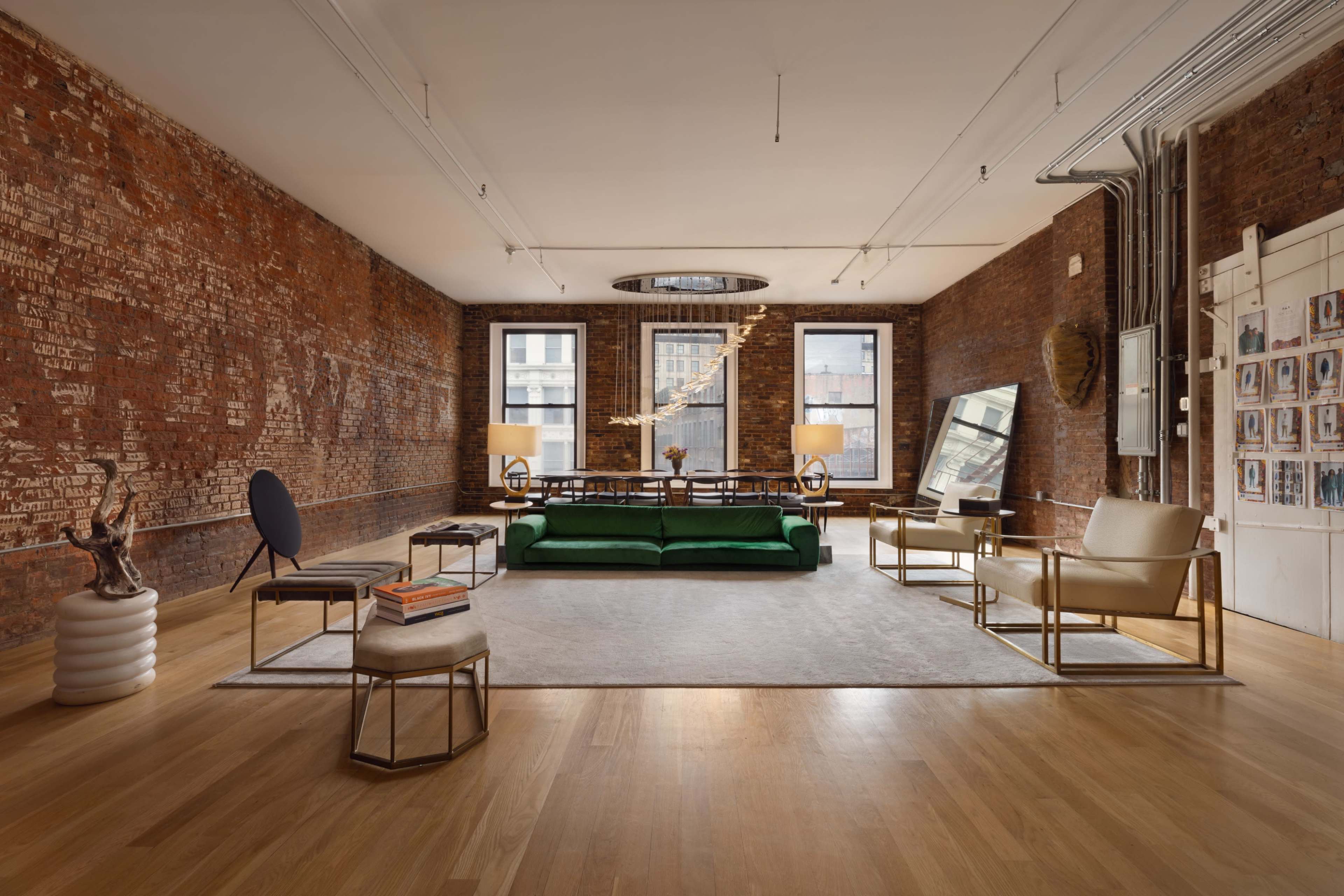 A spacious room with exposed brick walls, a green sofa, two armchairs, a round coffee table, and large windows letting in natural light.