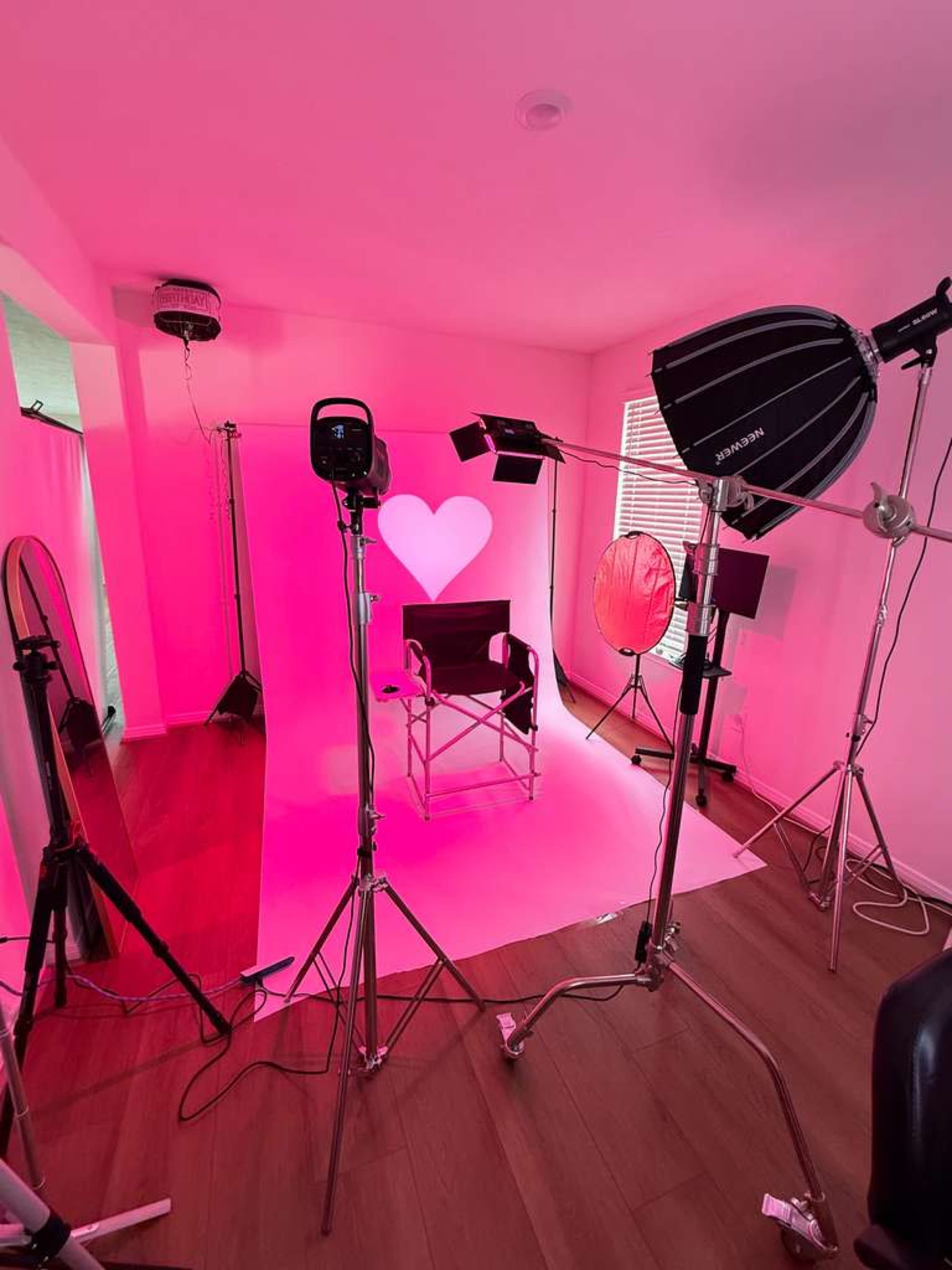 The image features a photography studio setup with various lighting equipment arranged around a chair, against a pink backdrop with a heart shape illuminated.