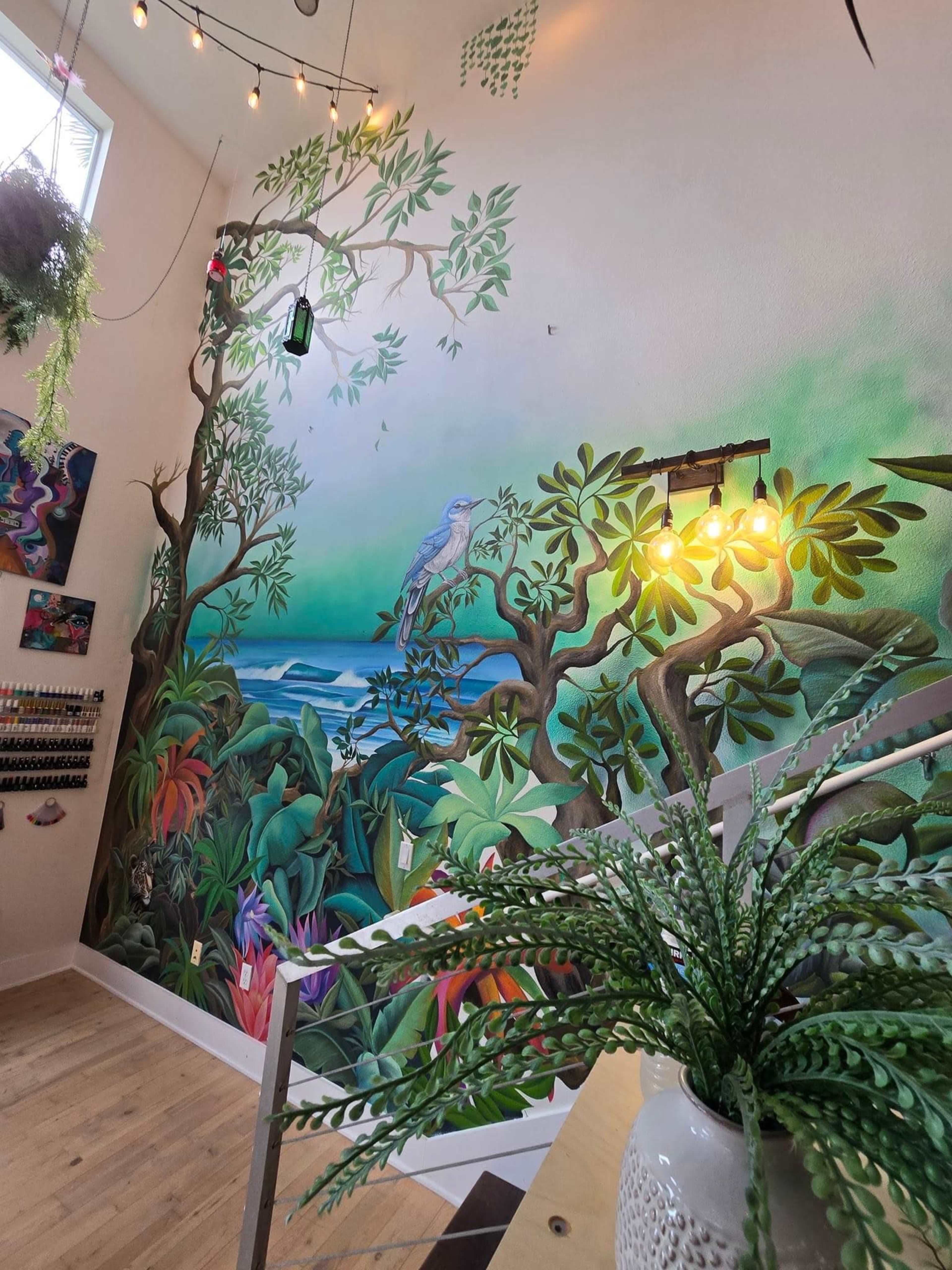 A vibrant mural of trees and a blue bird against a backdrop of ocean and greenery, illuminated by decorative lights.