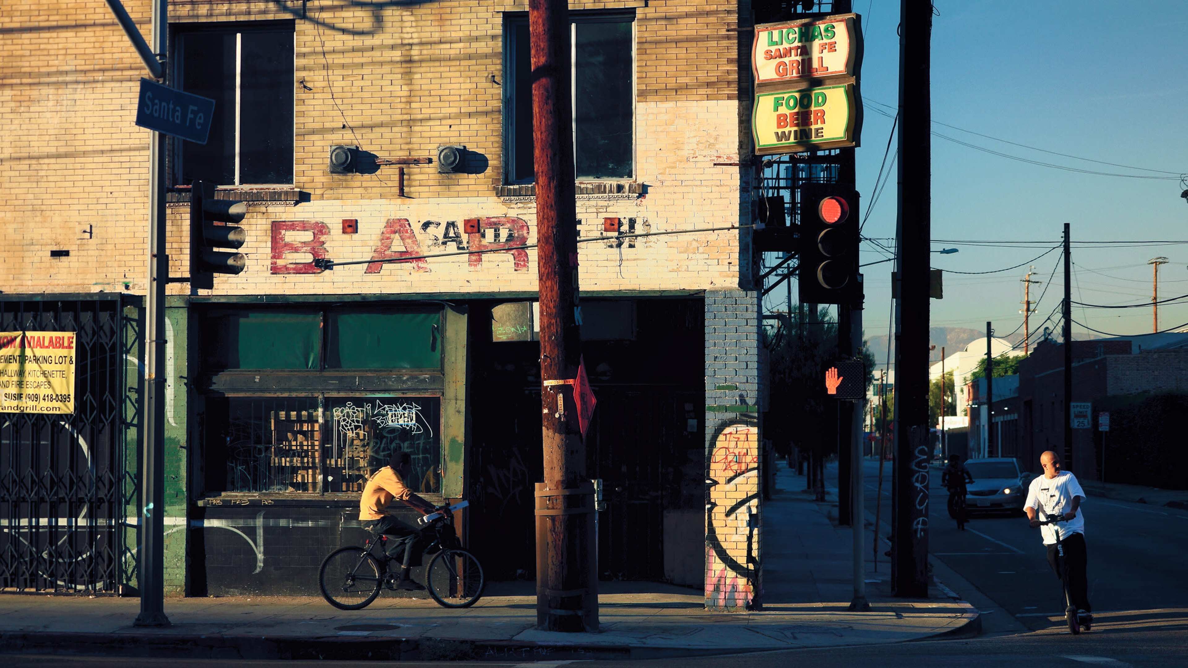 A cyclist rides past a weathered bar with a faded sign and a traffic light in an urban setting.