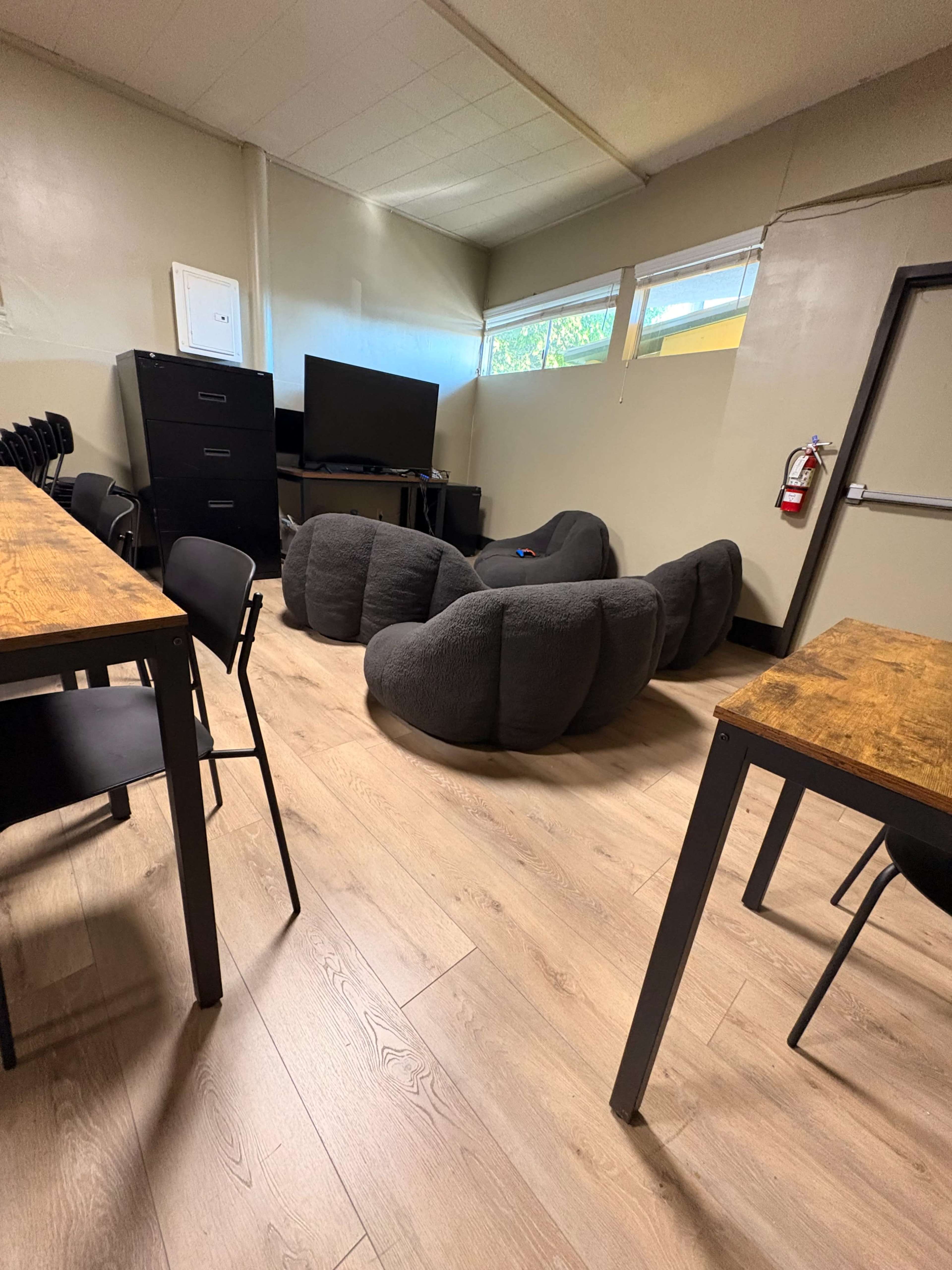 The room features several black chairs and tables arranged near a group of oversized, bean-shaped seating cushions, along with a large television against one wall.