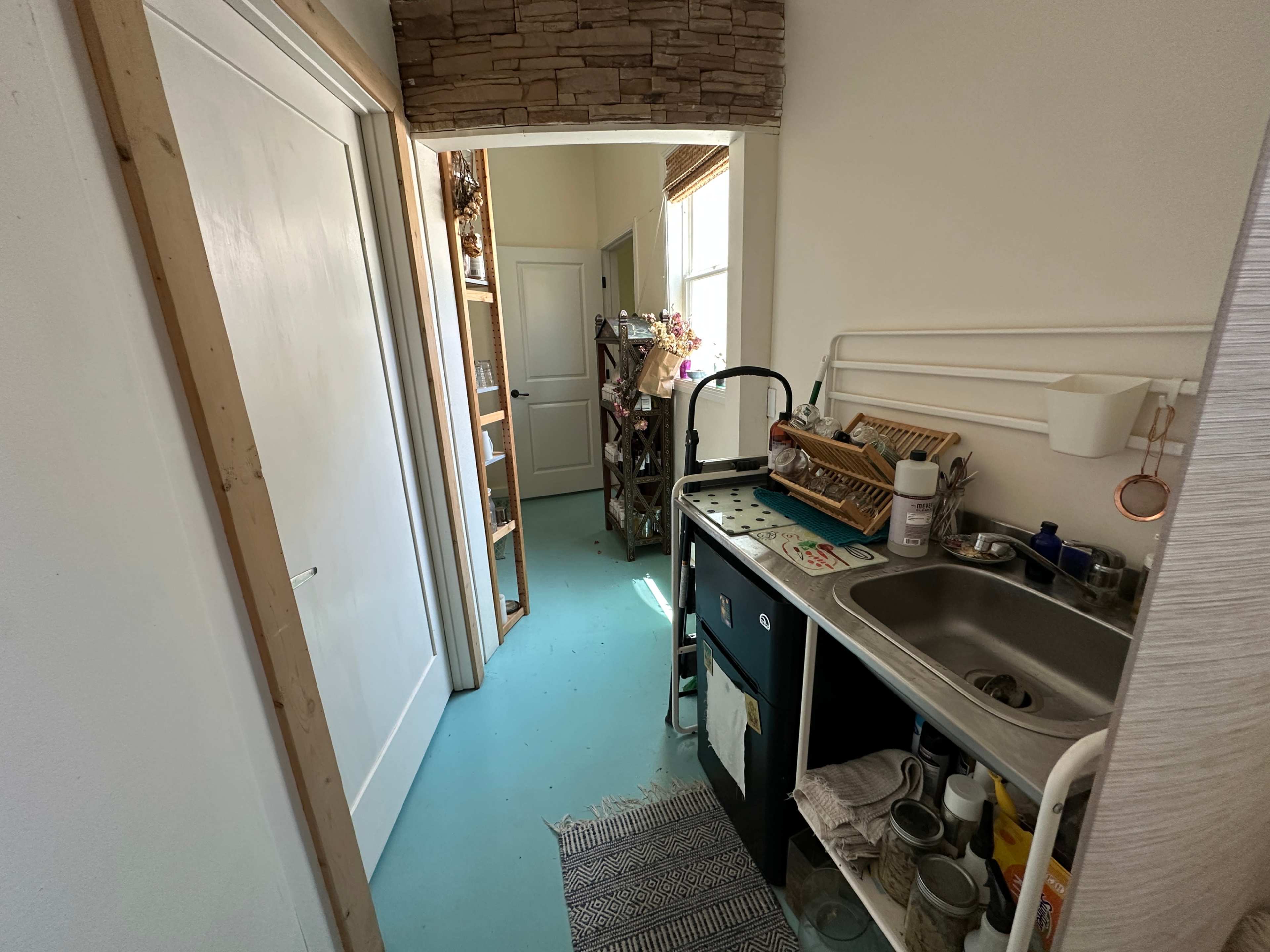 The image shows a narrow kitchen area with a sink, countertop, and various kitchen items, leading into a hallway with doors on either side.