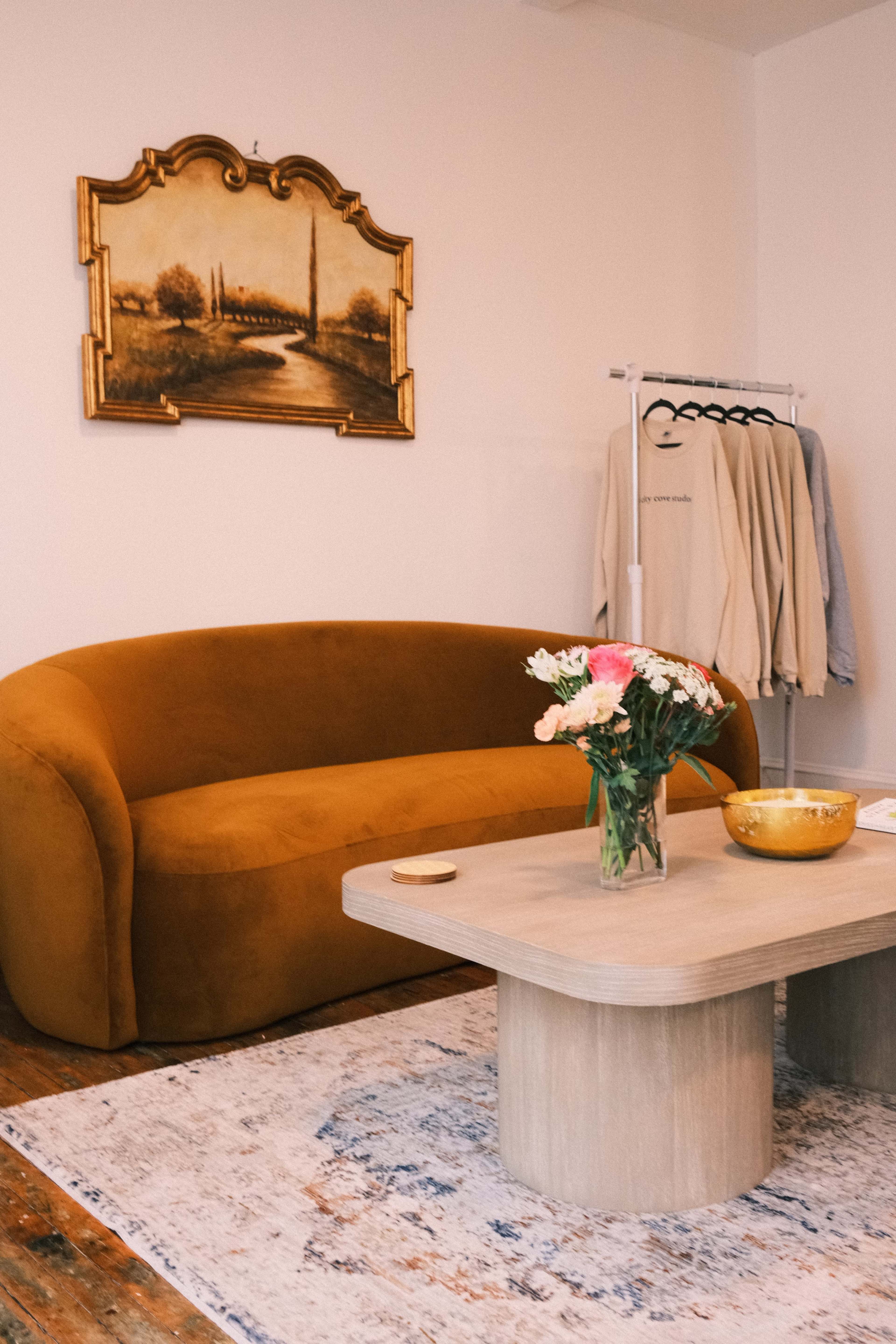 The image features a cozy living room with a brown curved sofa, a wooden coffee table, a vase of flowers, and a painting on the wall.