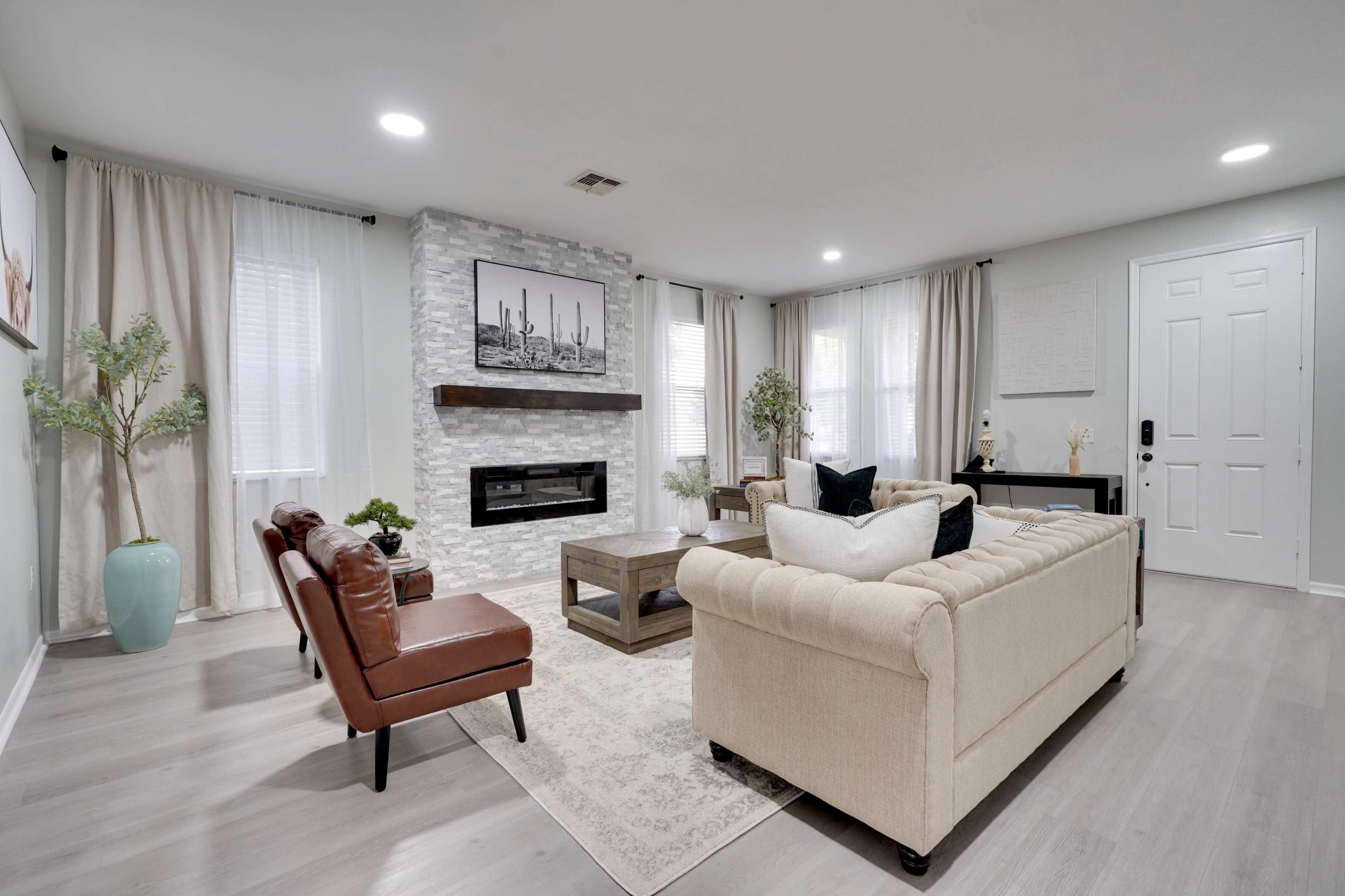 The living room features a light-colored sofa, a wooden coffee table, a modern fireplace, and large windows with sheer curtains.