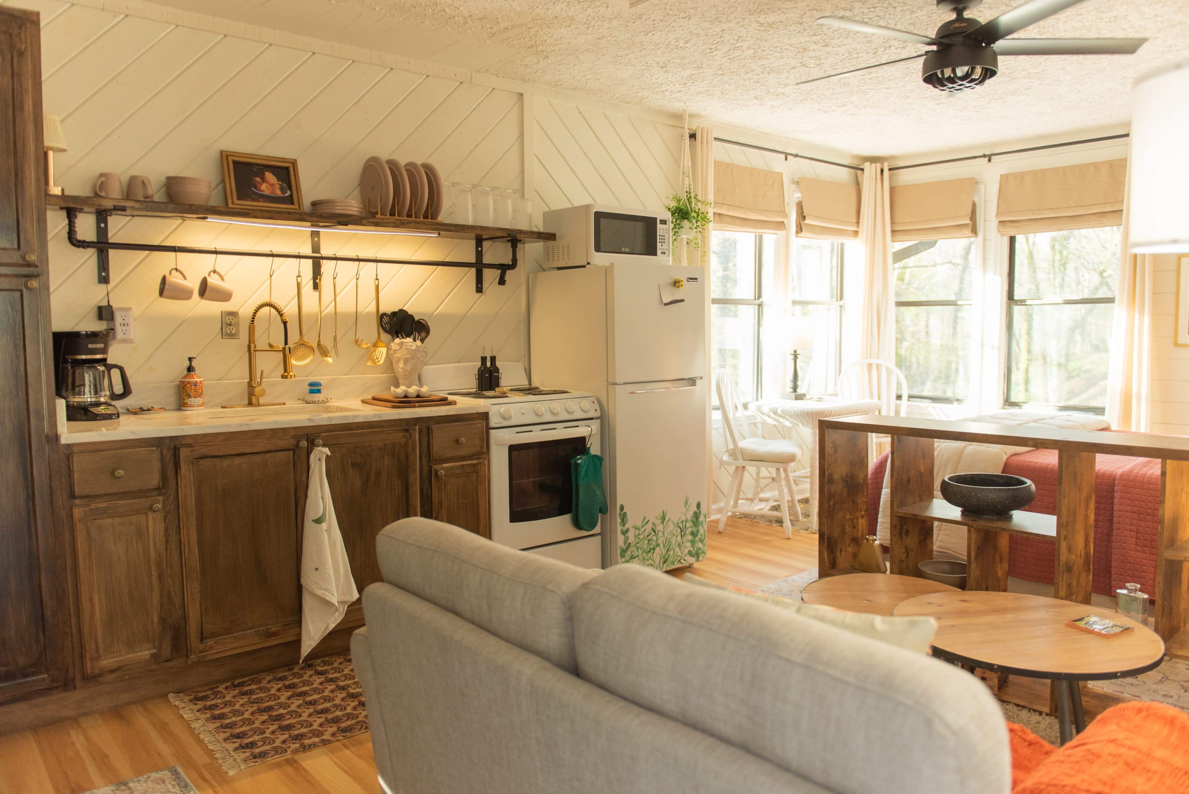 A cozy kitchen features a stove, fridge, sink, and countertop adorned with kitchenware, alongside a living area with a sofa and coffee table.