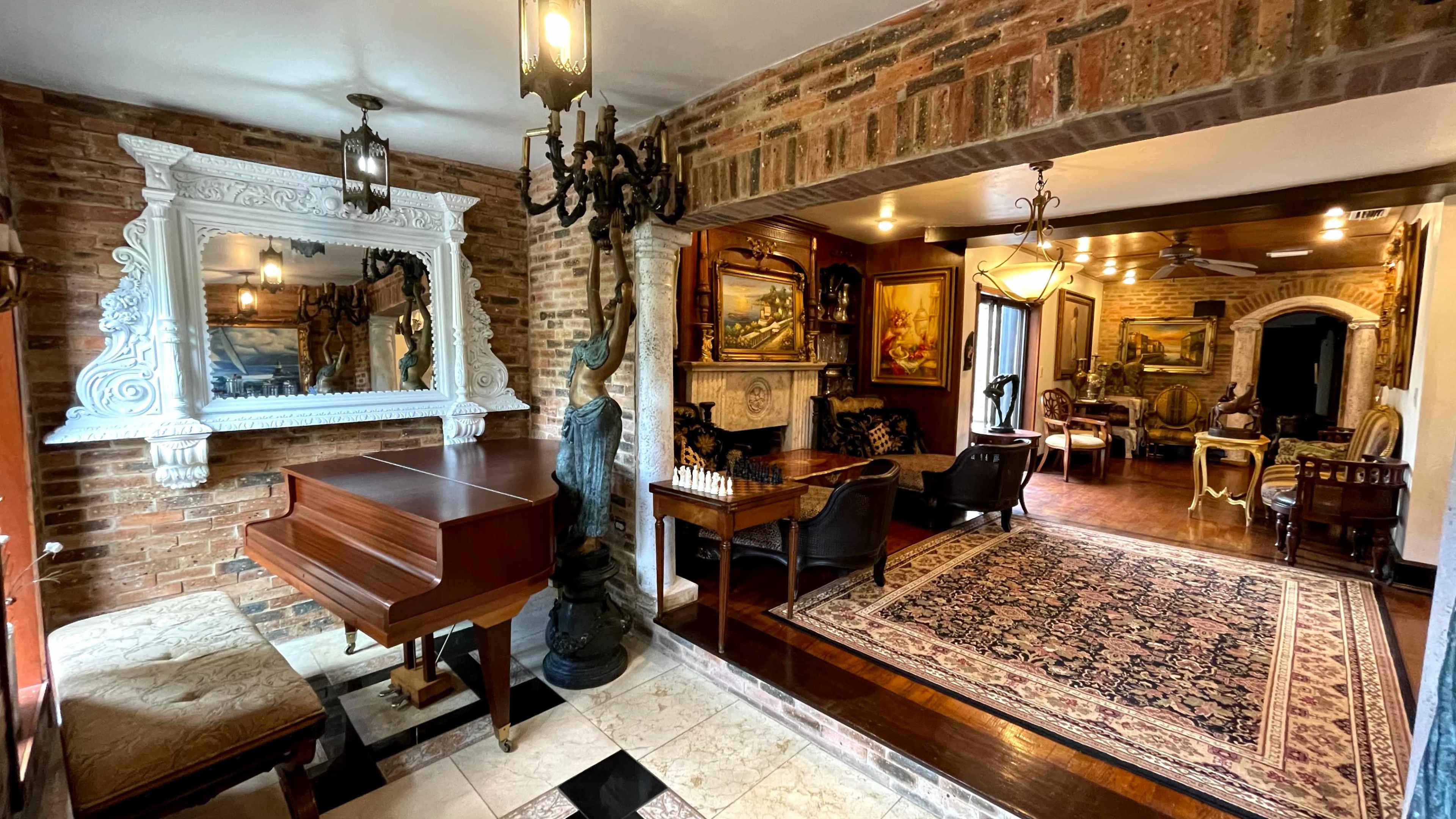 The image depicts an elegantly furnished room featuring a grand piano, ornate mirror, and various seating areas with decorative paintings on the walls.