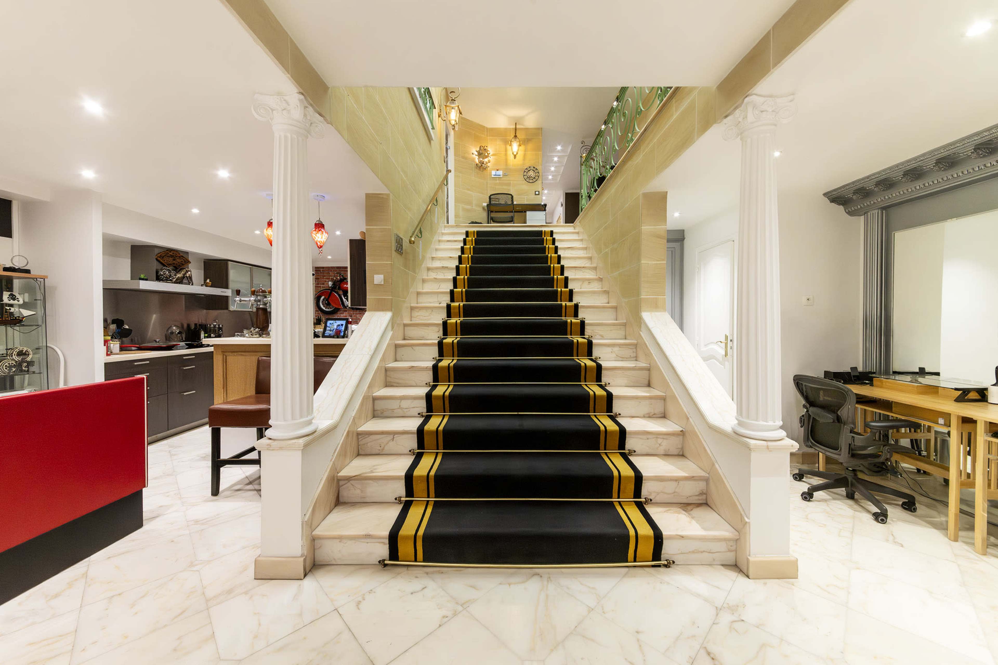 A staircase with a black carpet featuring yellow stripes, leading up to a well-lit upper floor, flanked by two white columns.