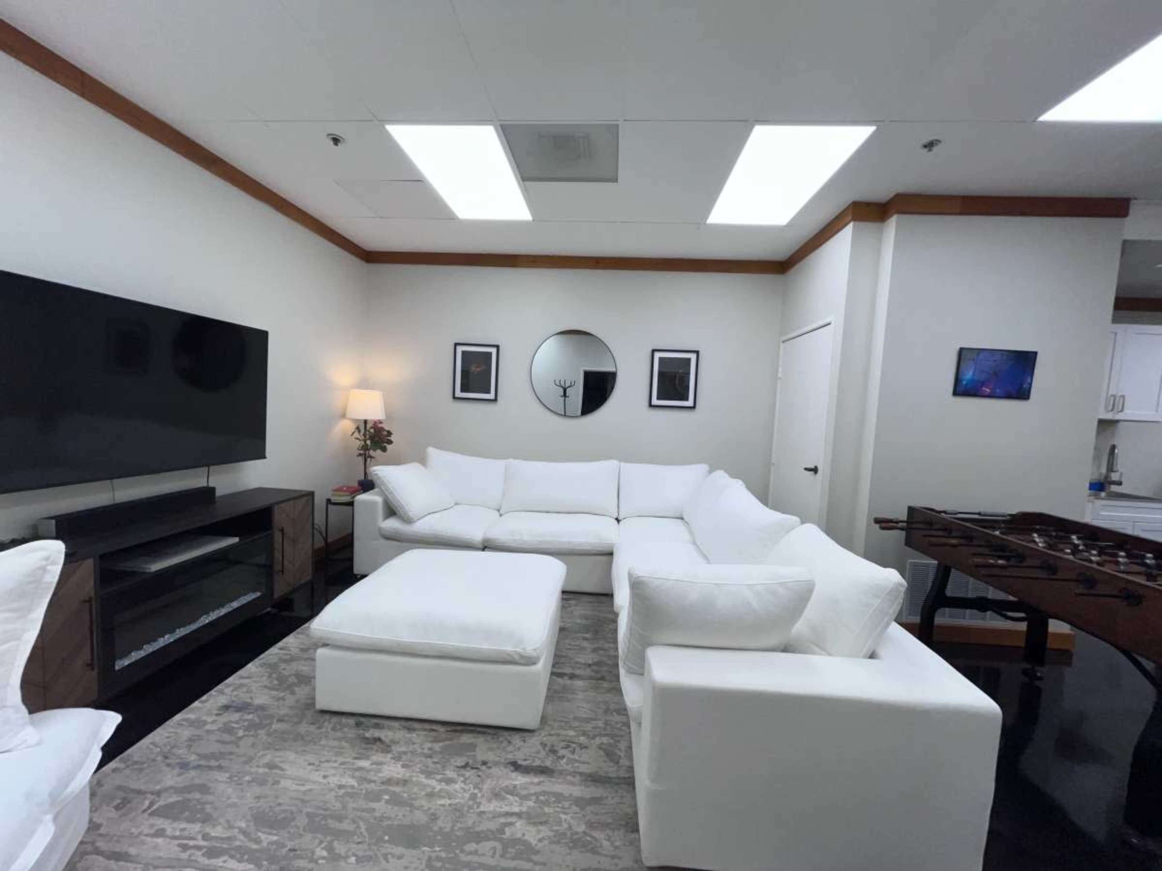The image shows a modern living room with a large white sectional sofa, a black television mounted on the wall, and a coffee table on a gray rug.