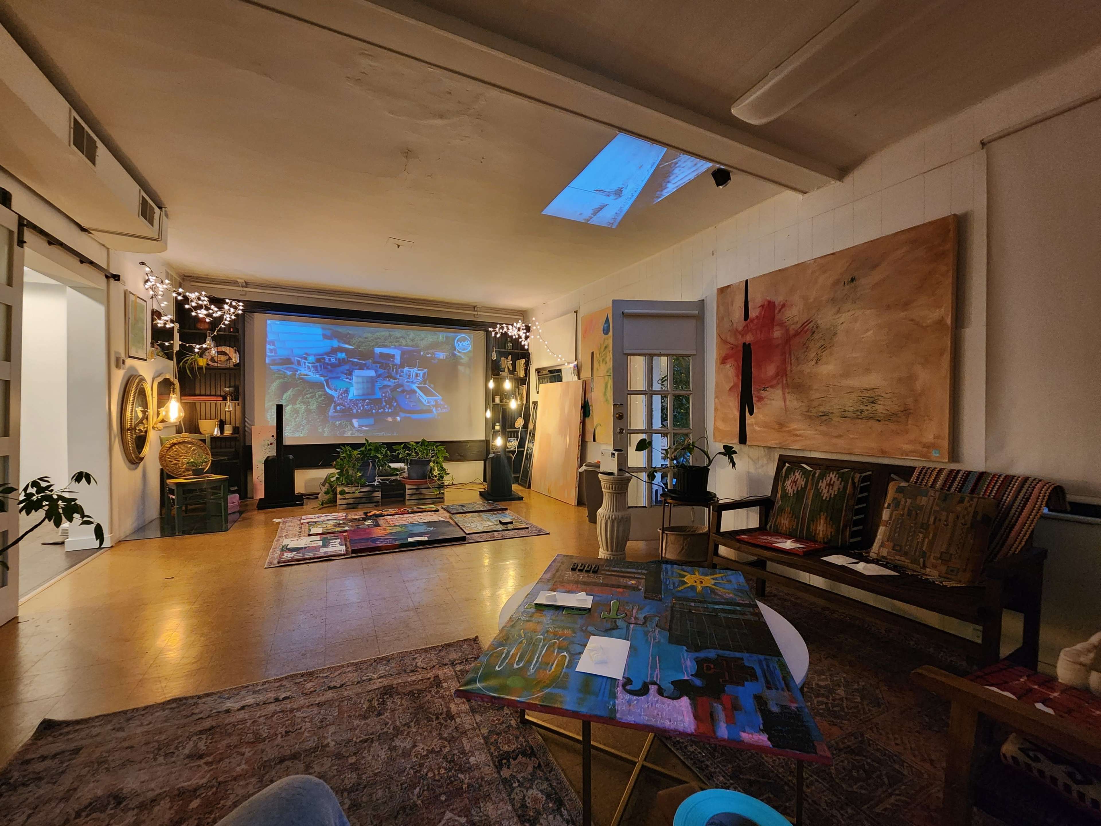 A spacious art studio with colorful artwork displayed on the walls and a large projector screen against one side.