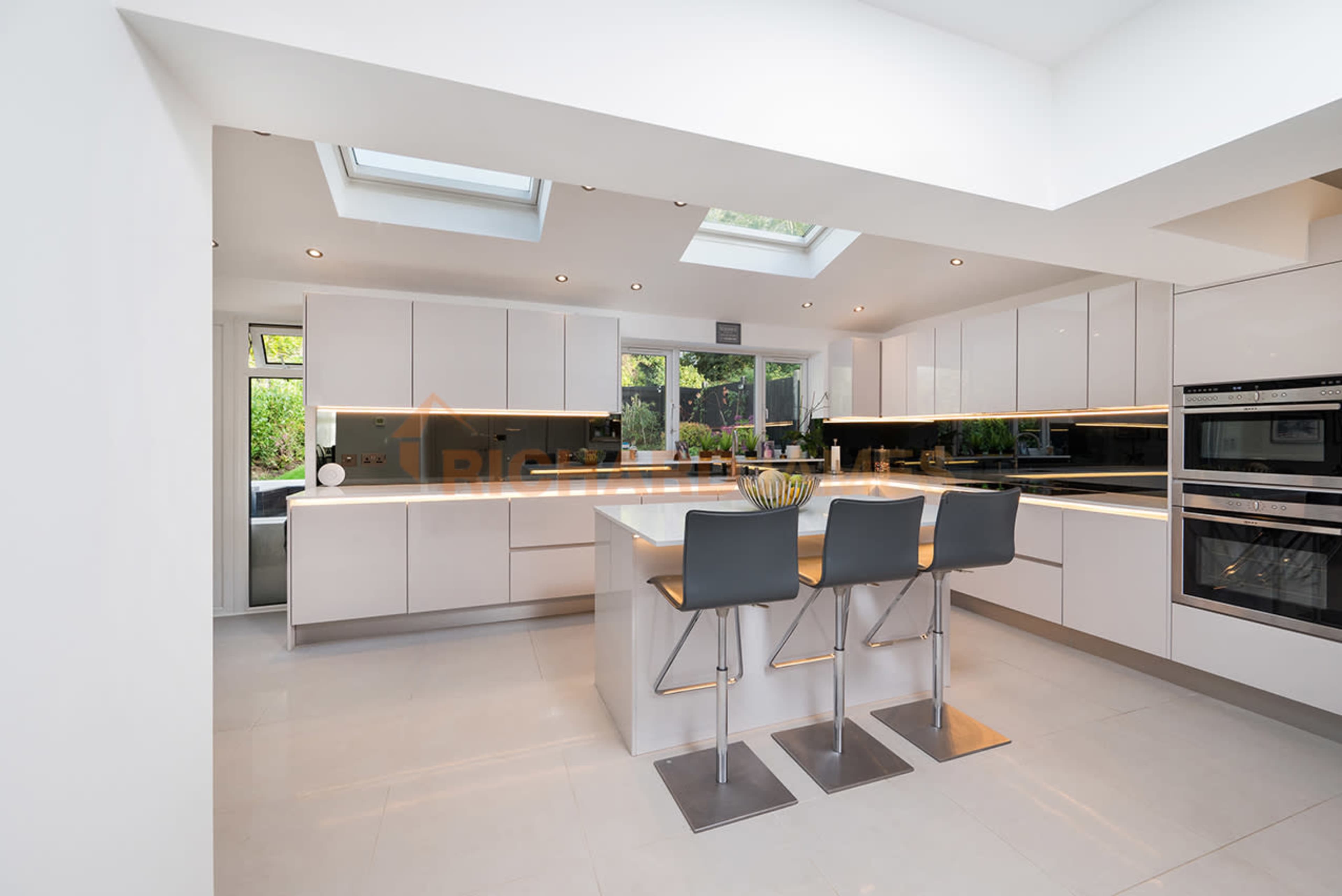 A modern kitchen featuring sleek cabinetry, a central island with bar seating, and large skylights that provide natural light.