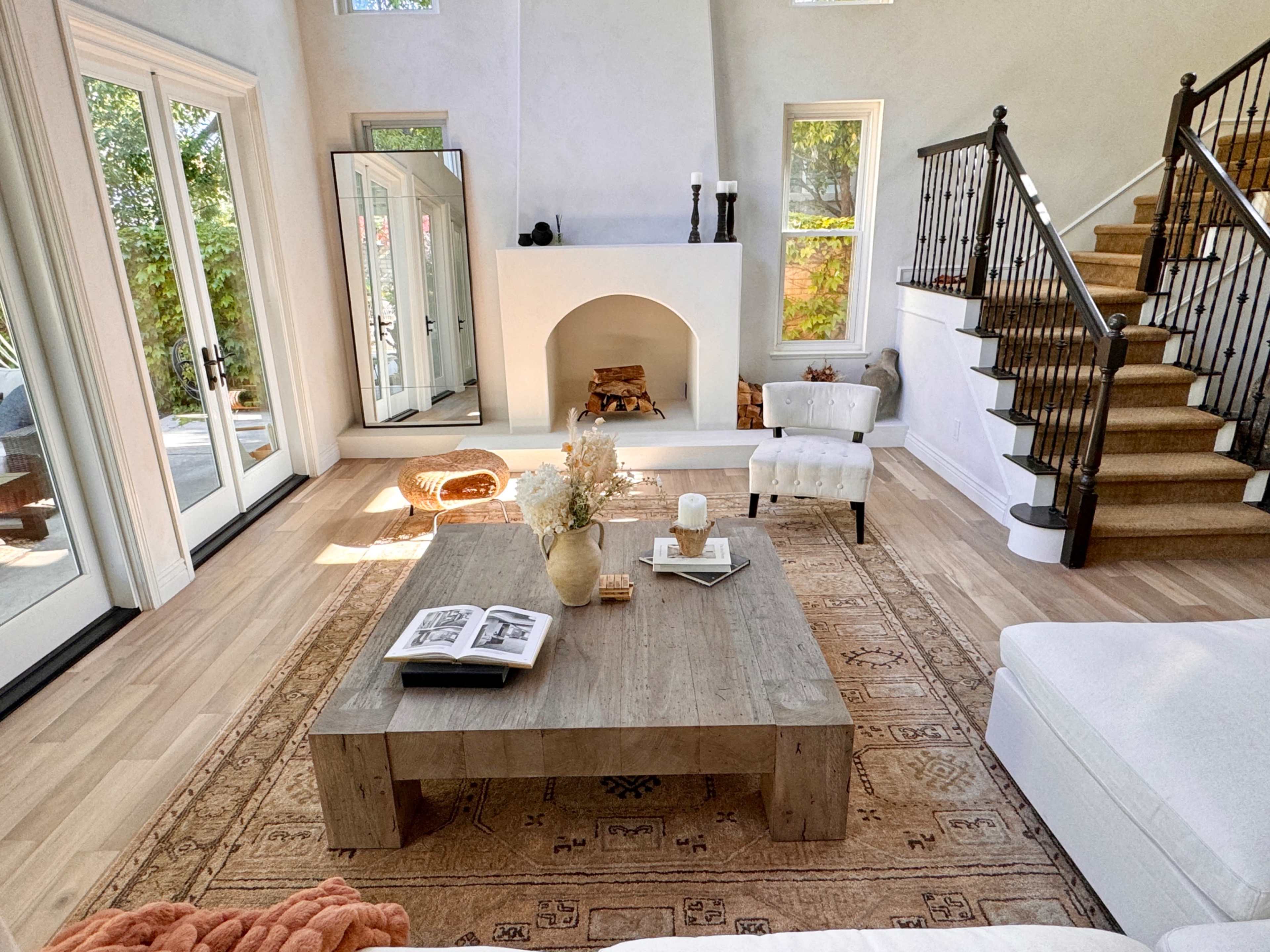 A modern living room with a wooden coffee table, a white sofa, a rug on the floor, and a staircase in the background.
