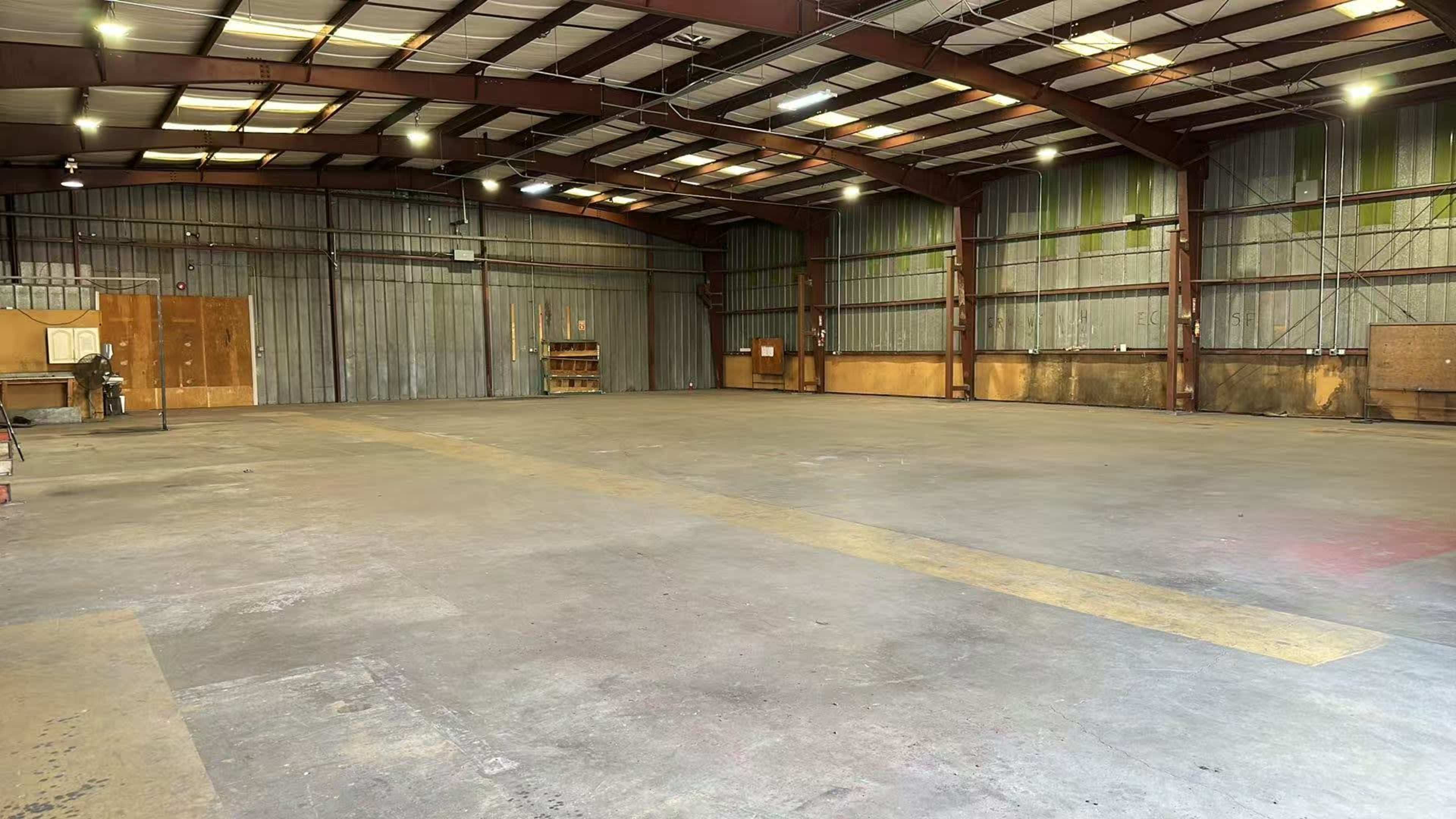 The image shows a large industrial warehouse with a steel frame, clear concrete floor, and high ceilings.