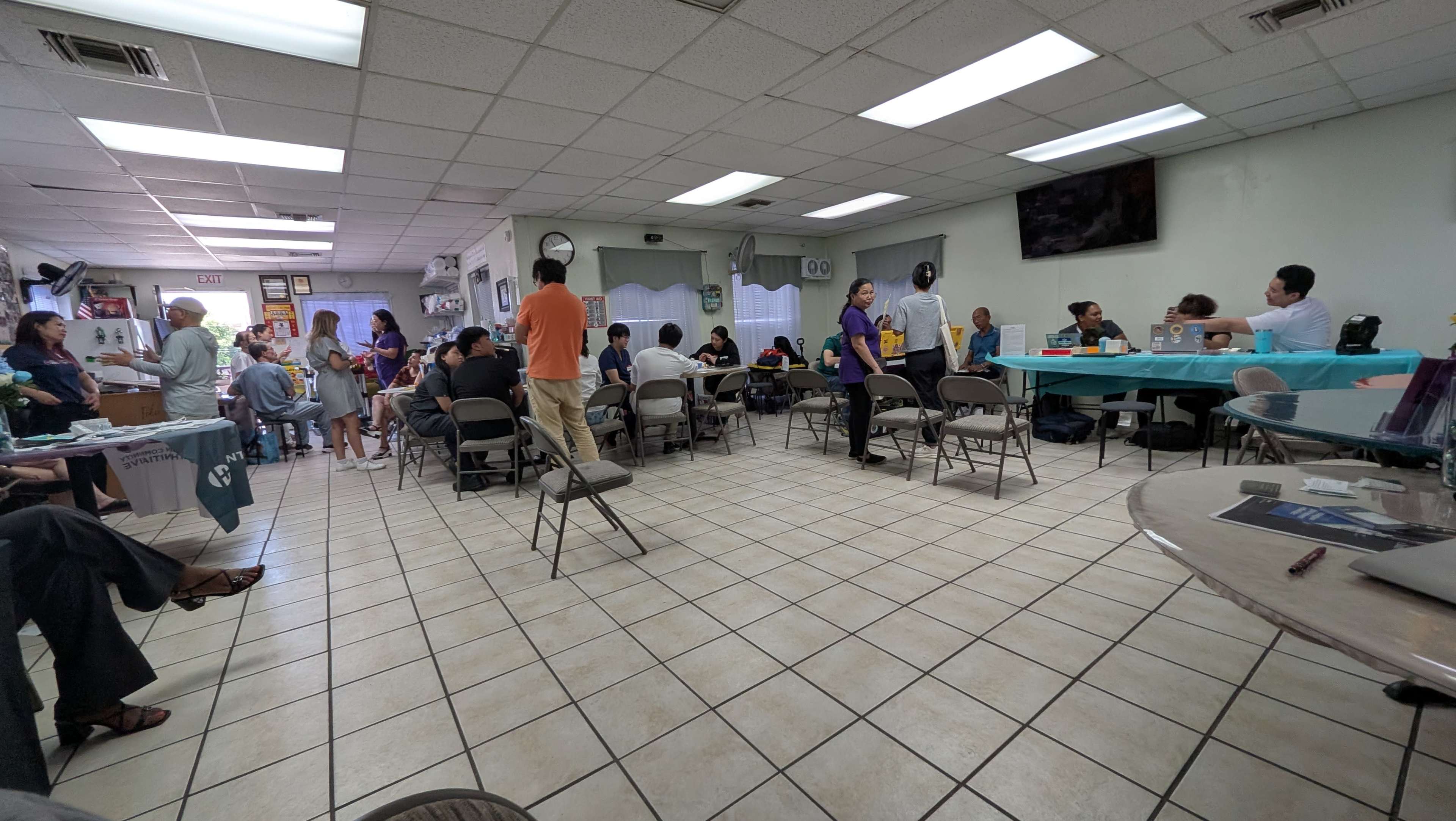 A group of people is gathered in a spacious room with tables and chairs, engaging in various activities and conversations.