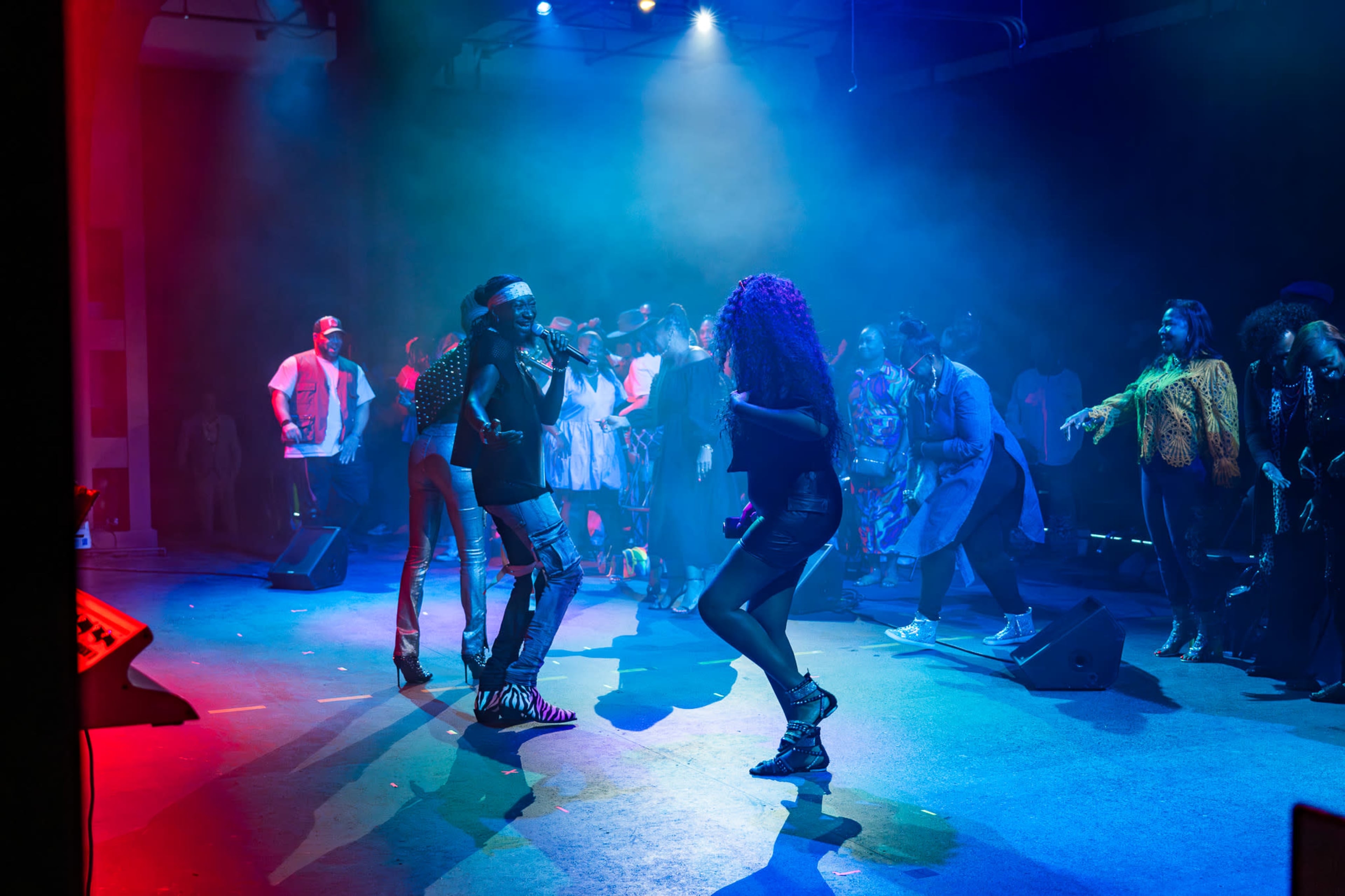 A performer sings on stage while audience members dance and engage with the music in a dimly lit venue.