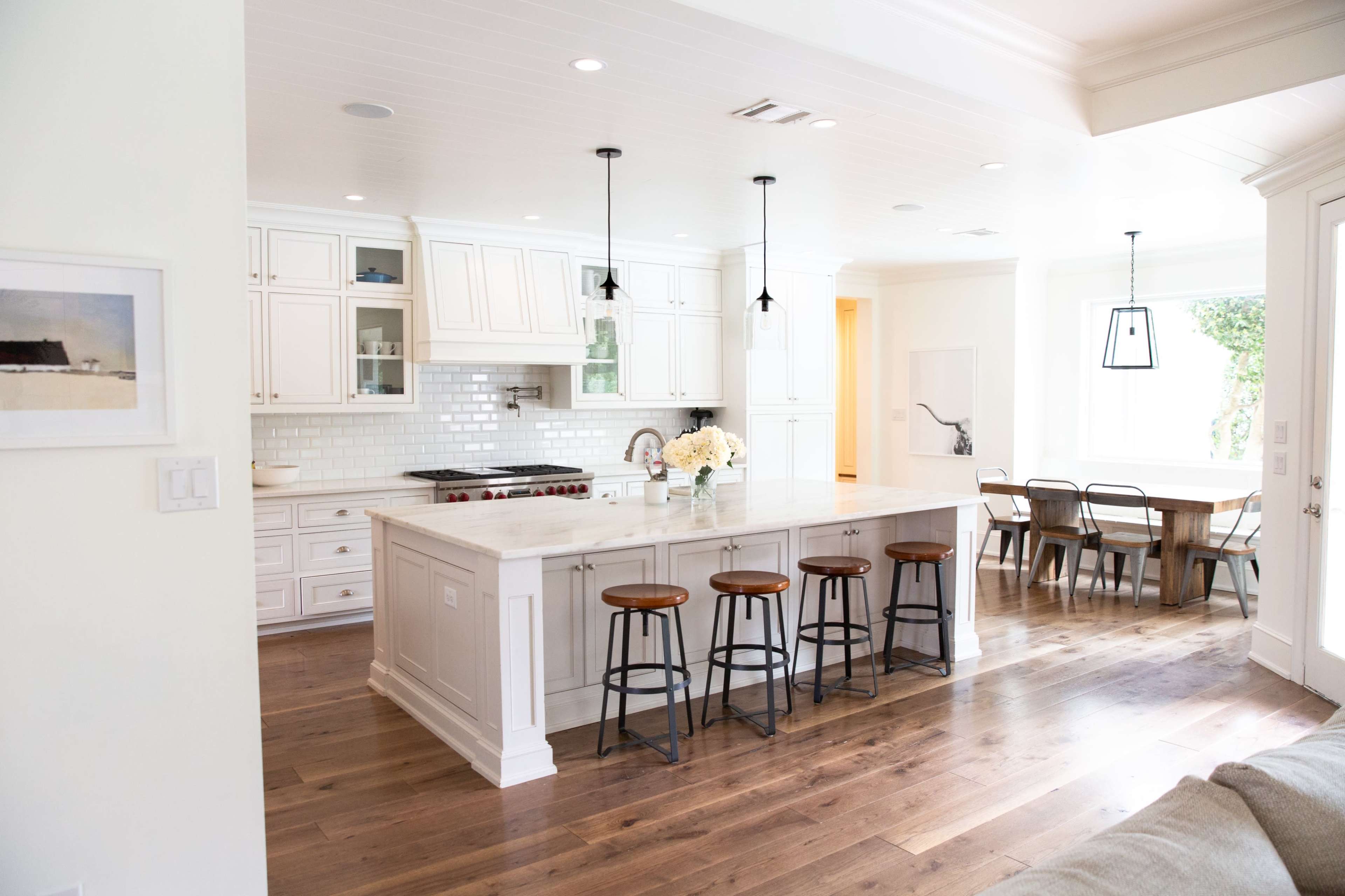 A modern kitchen with white cabinetry, a large marble island with bar stools, and an adjacent dining area with a wooden table and chairs.