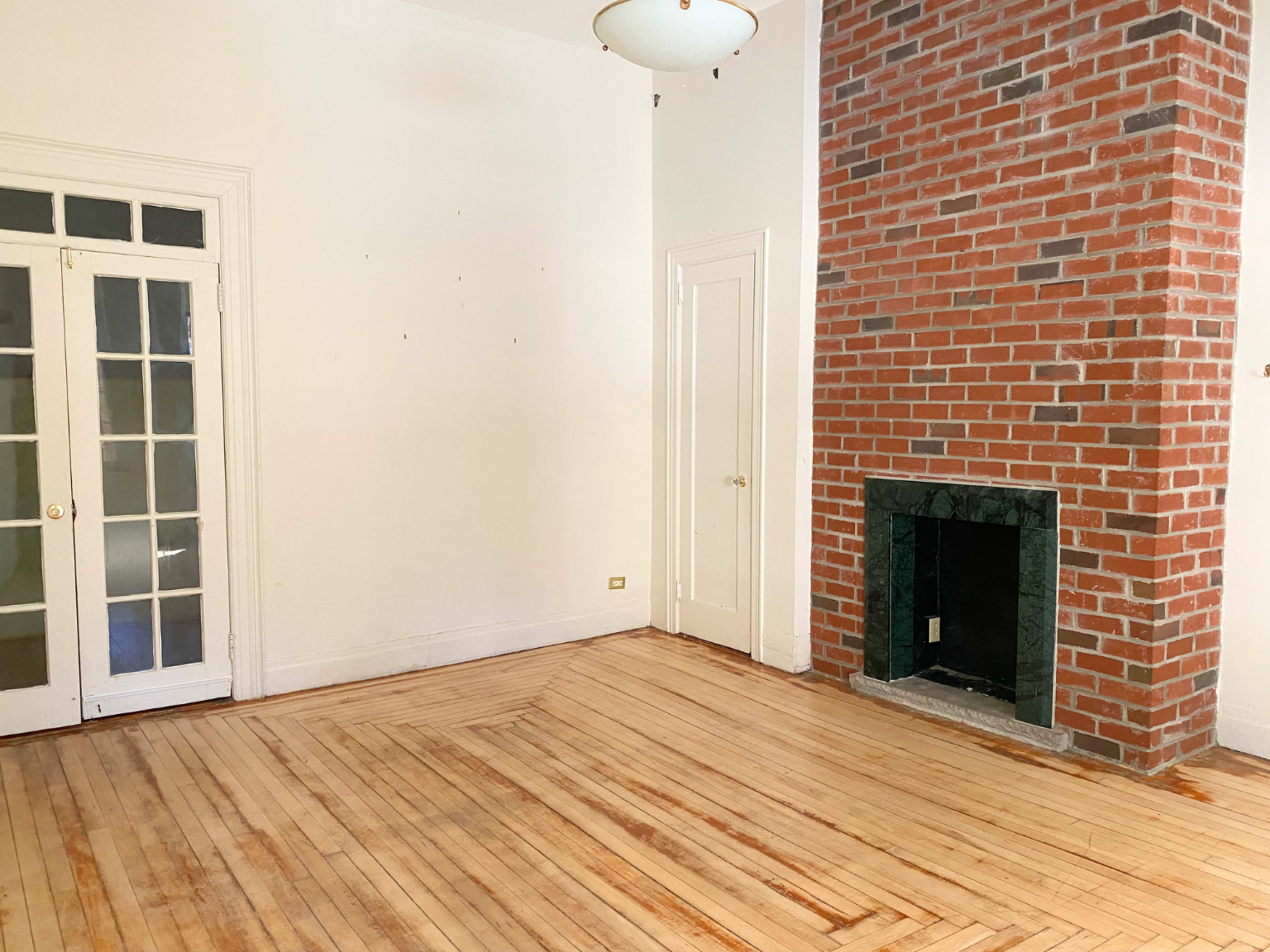 The image shows a room with hardwood floors, a brick fireplace, and large glass-paneled doors leading to another space.