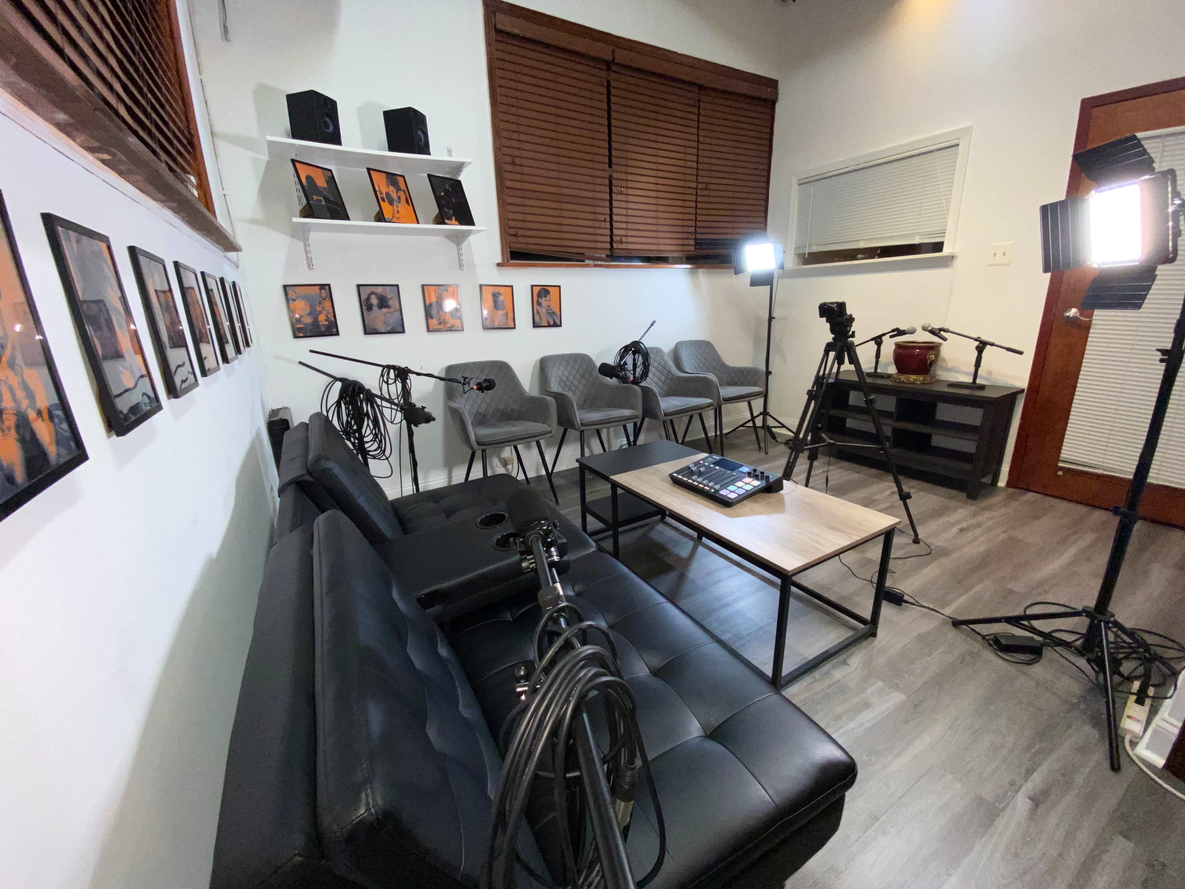 The image shows a modern room with a black couch, a coffee table, multiple microphones on stands, and several photography lights set up around empty gray chairs.