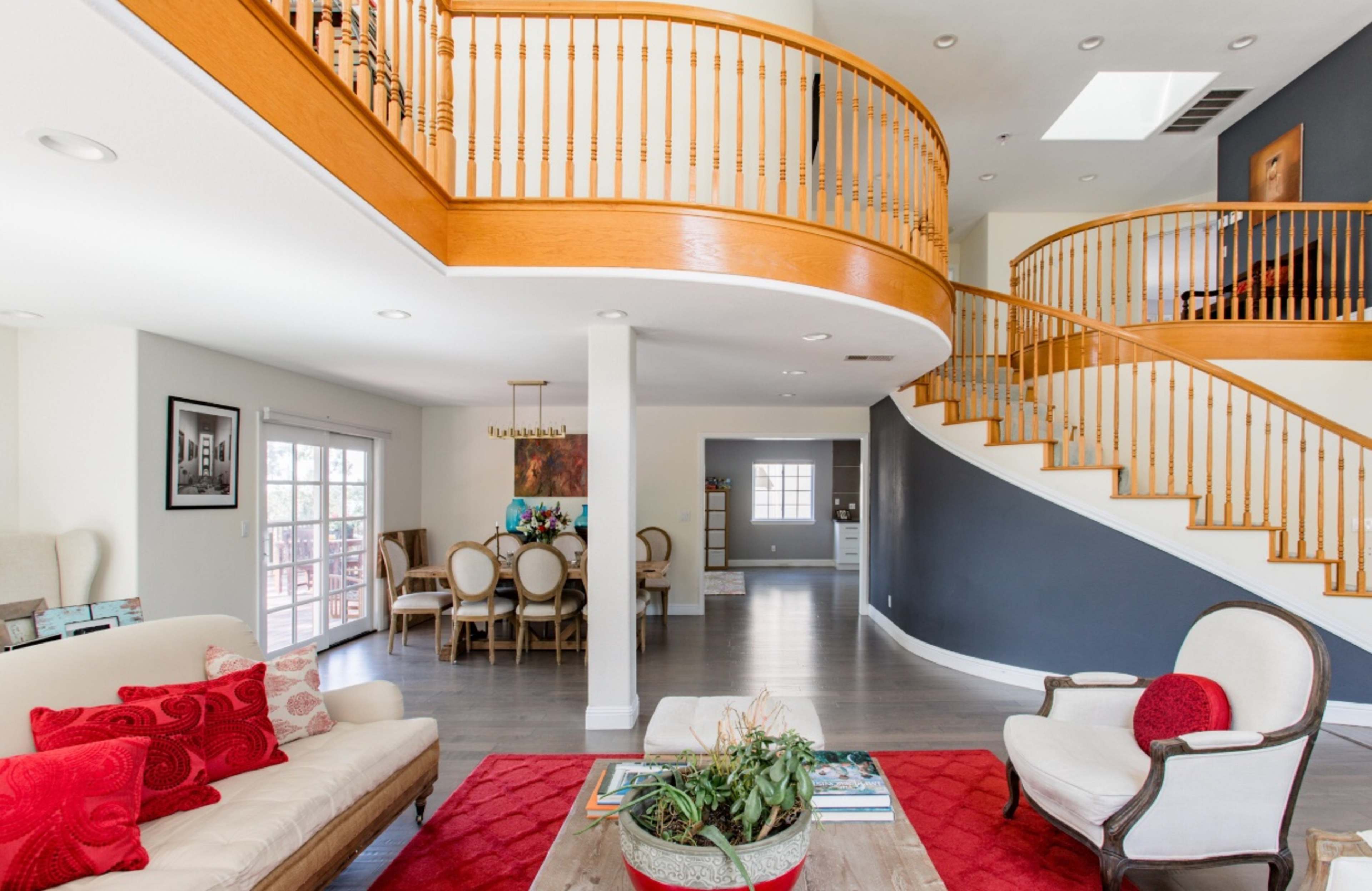 A spacious living area with a wooden staircase leading to an upper level, featuring a seating area with a couch and armchair on a red rug.