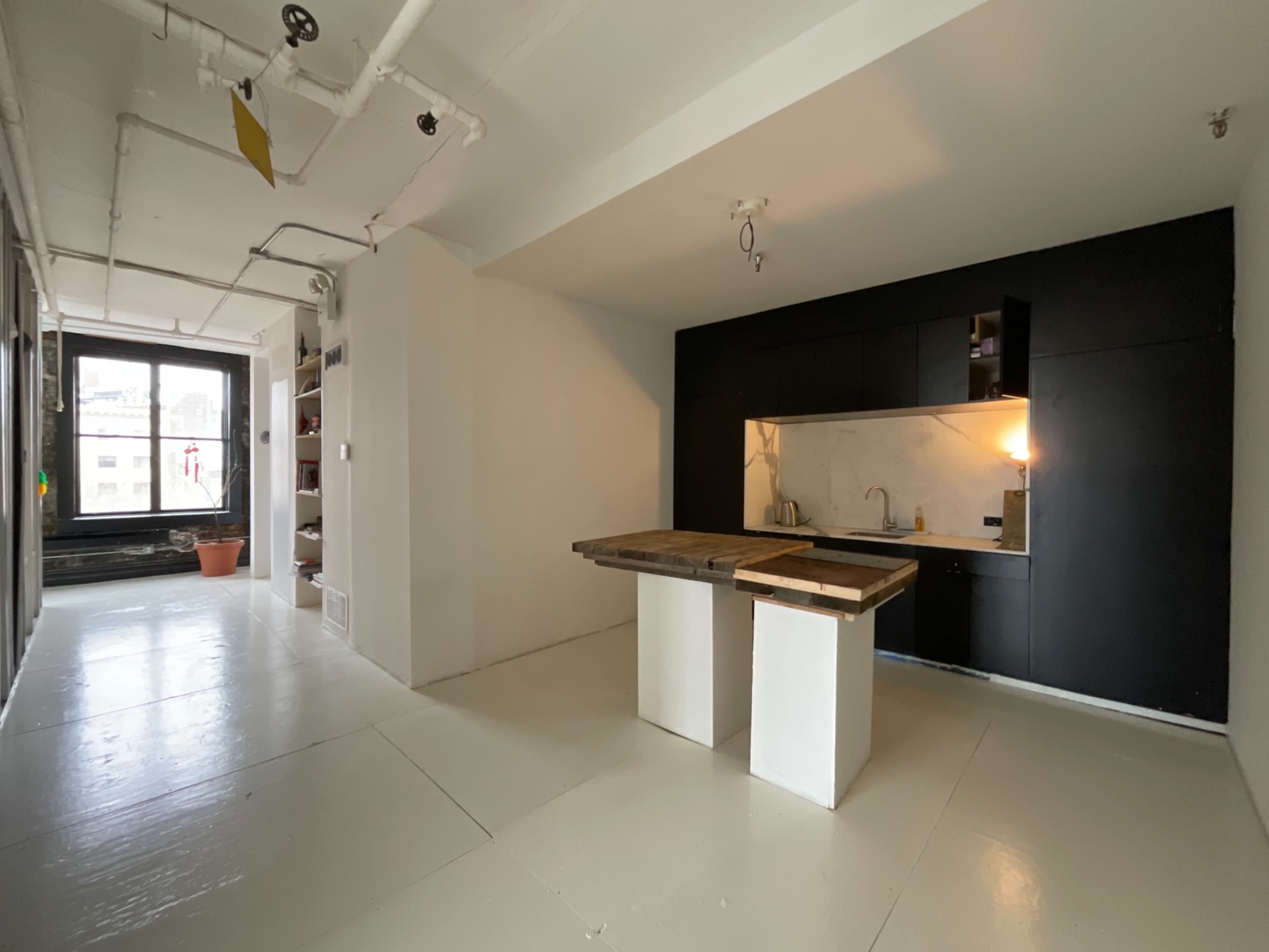 A minimalist kitchen features a wooden table and dark cabinetry against white walls in a bright, open space.