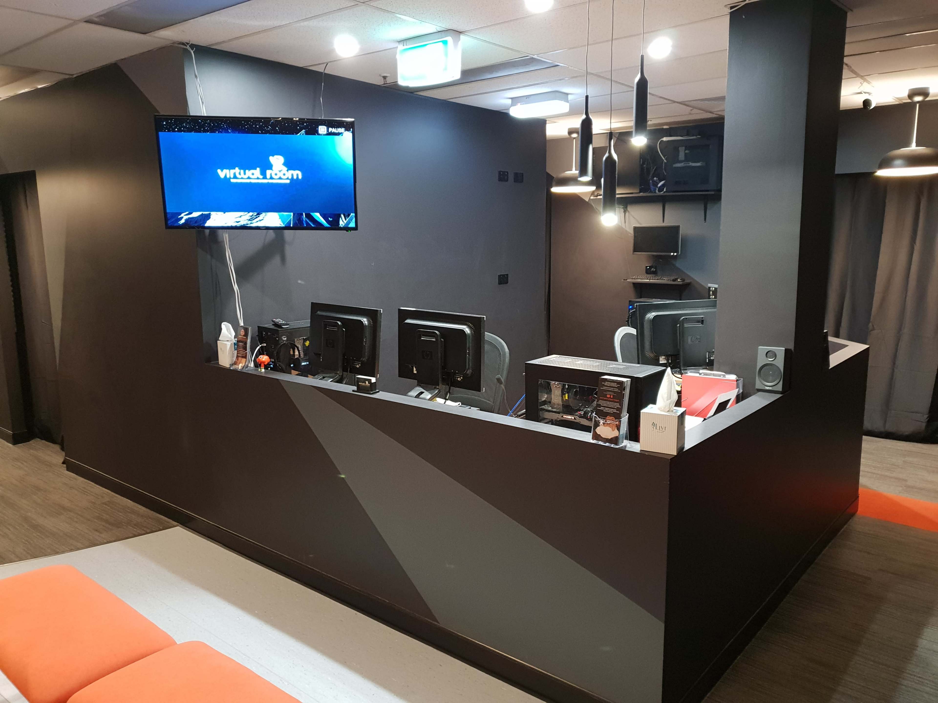 A modern interior of an entertainment space with multiple computer stations and a large screen displaying "virtual room."