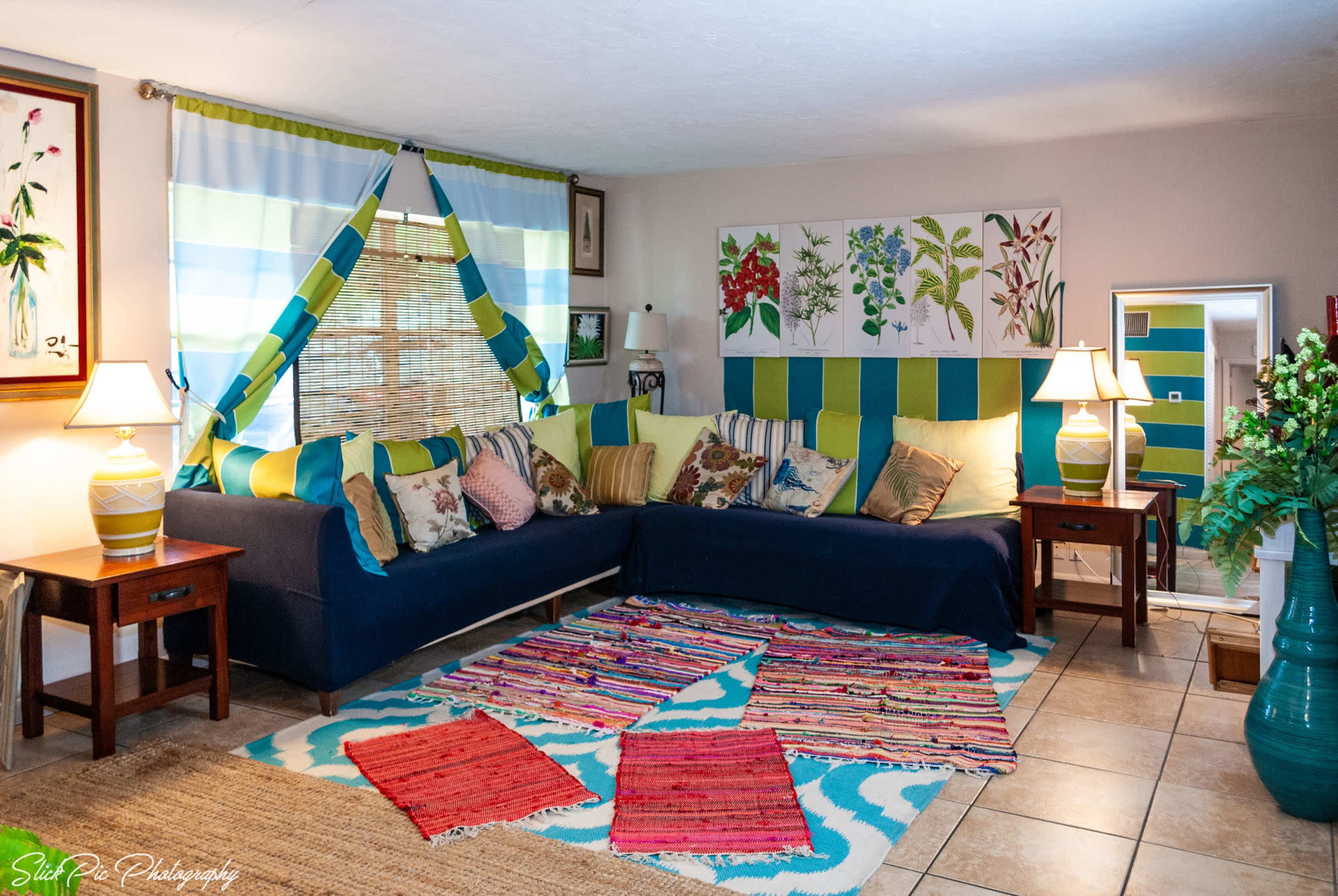 The image shows a cozy living room with a sectional couch, colorful pillows, a patterned rug, and decorative artwork on the walls.