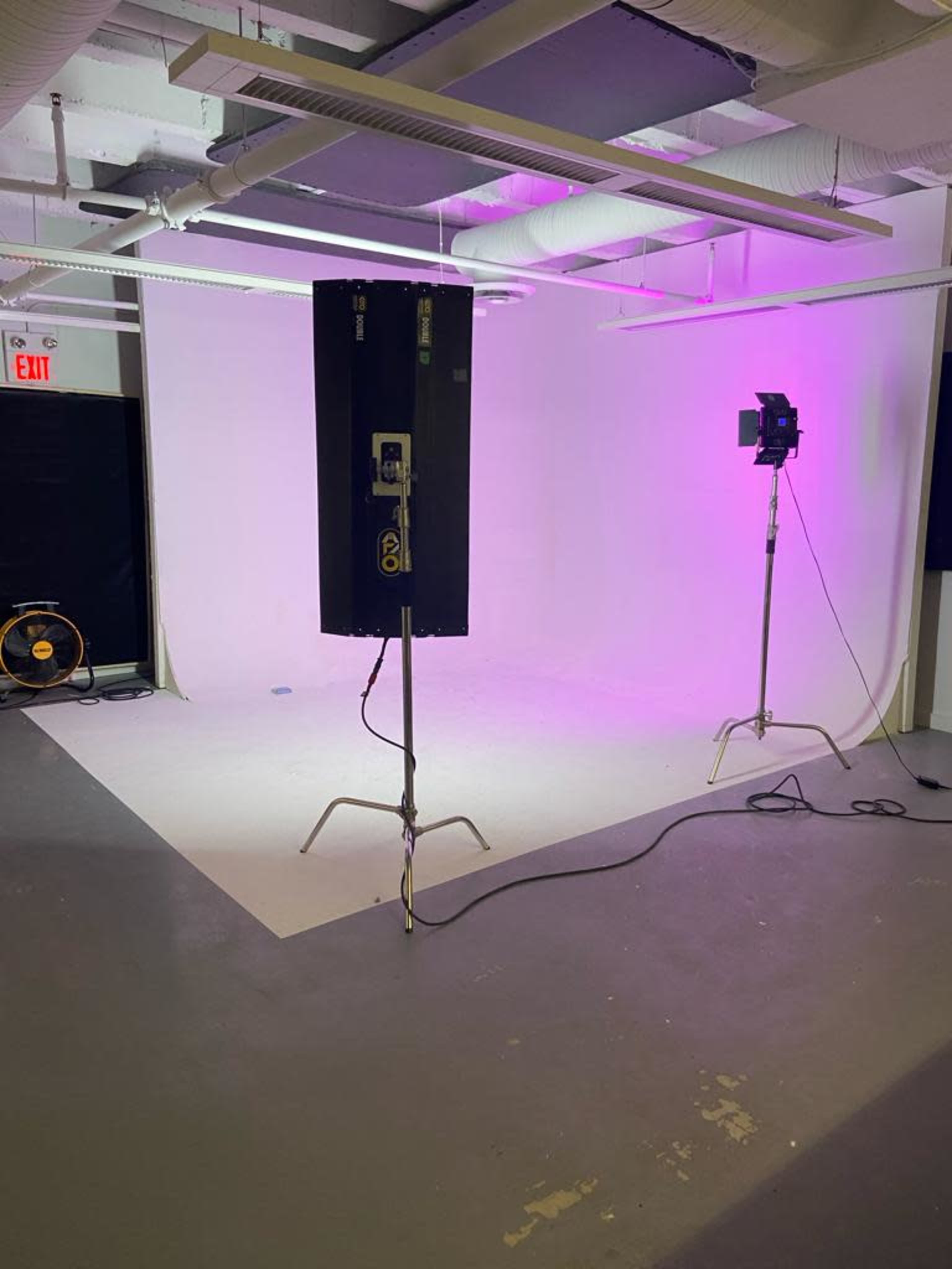 A photography studio with a plain backdrop, two lighting fixtures, and a floor fan.