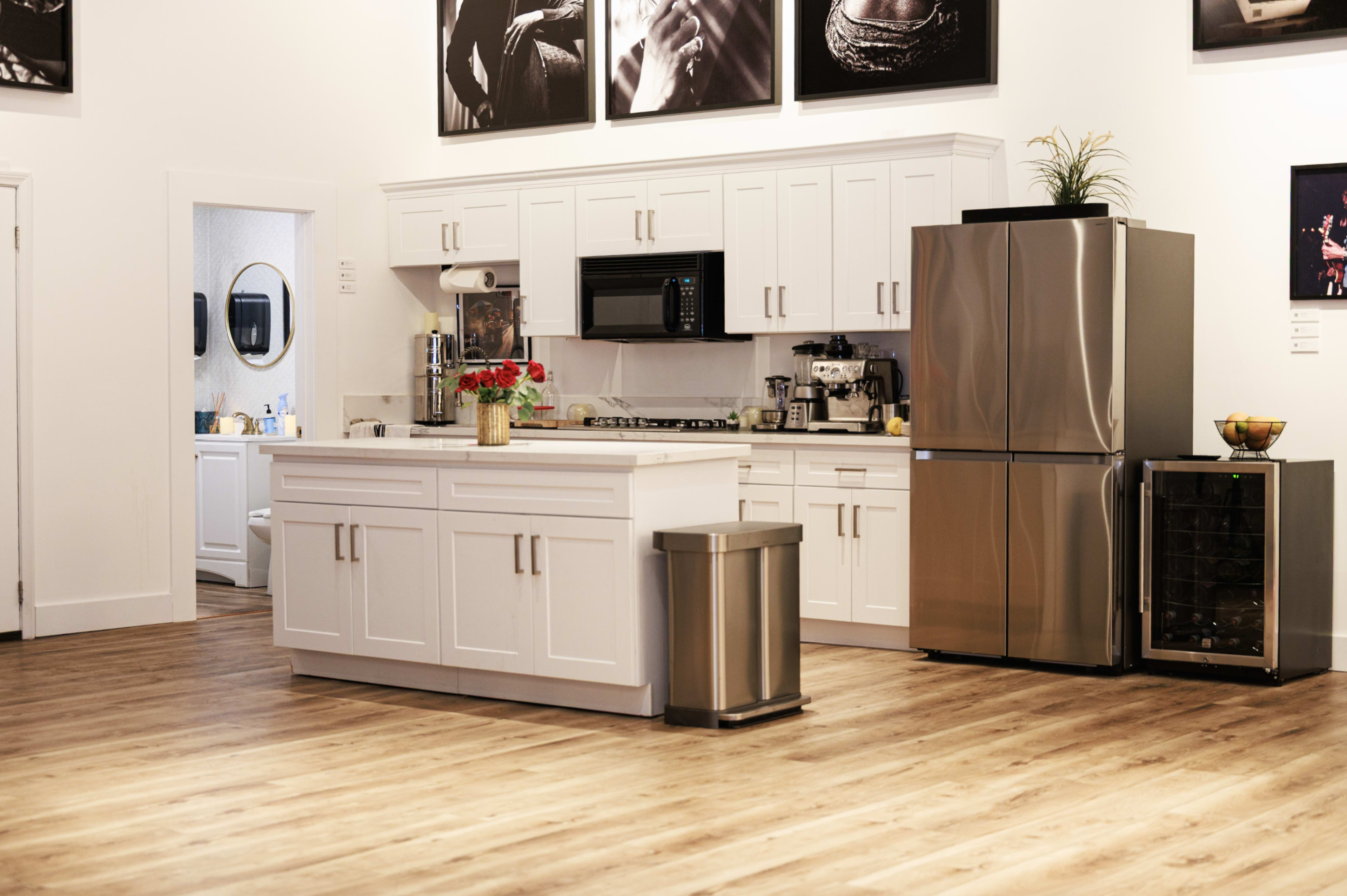 The image features a modern kitchen with white cabinetry, stainless steel appliances, and wooden flooring, accompanied by a decorative arrangement of flowers on the countertop.