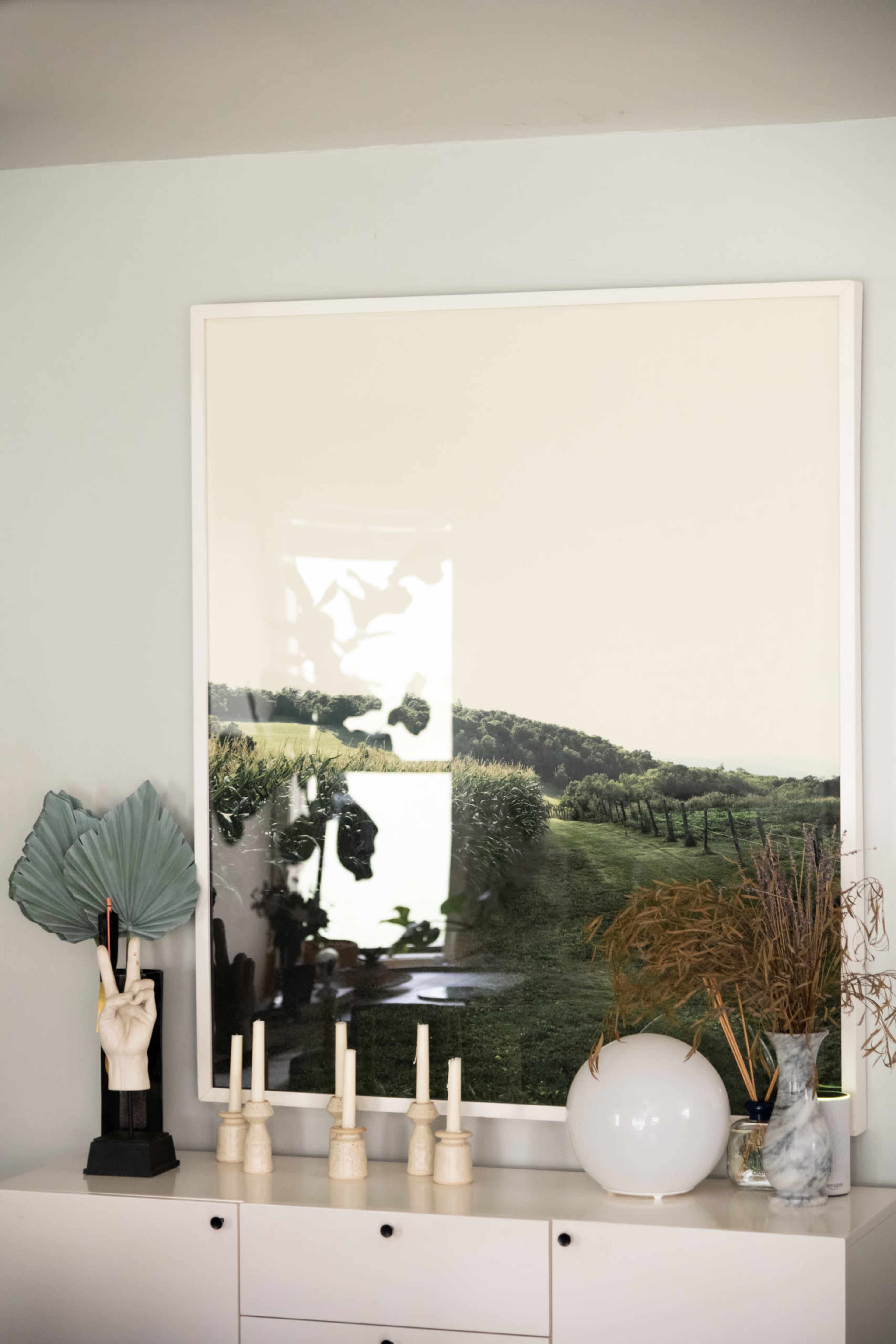 A large landscape photograph hangs on a wall above a minimalist console table adorned with decorative items and plants.