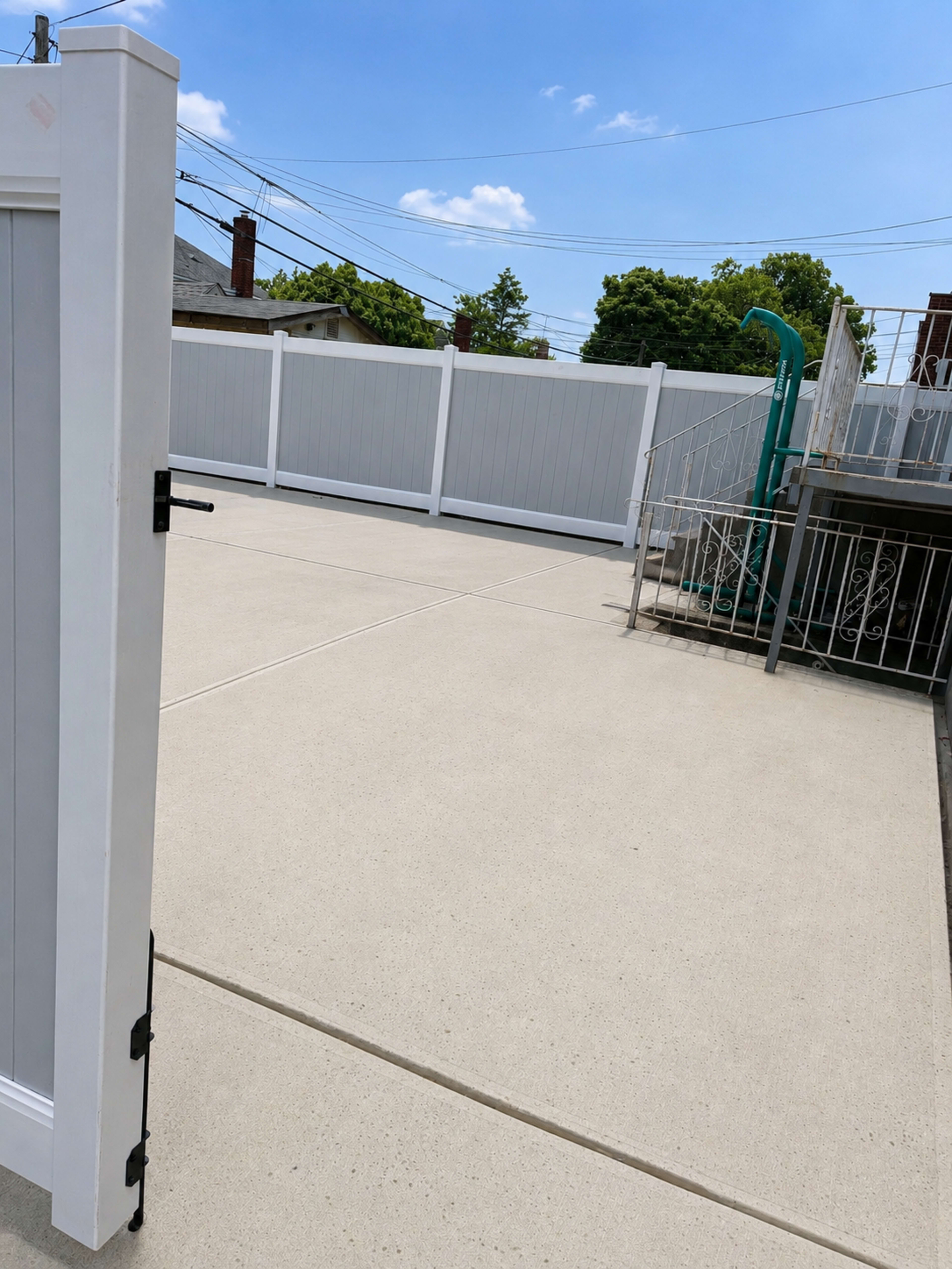 A white gate opens to a concrete patio enclosed by a tall privacy fence.