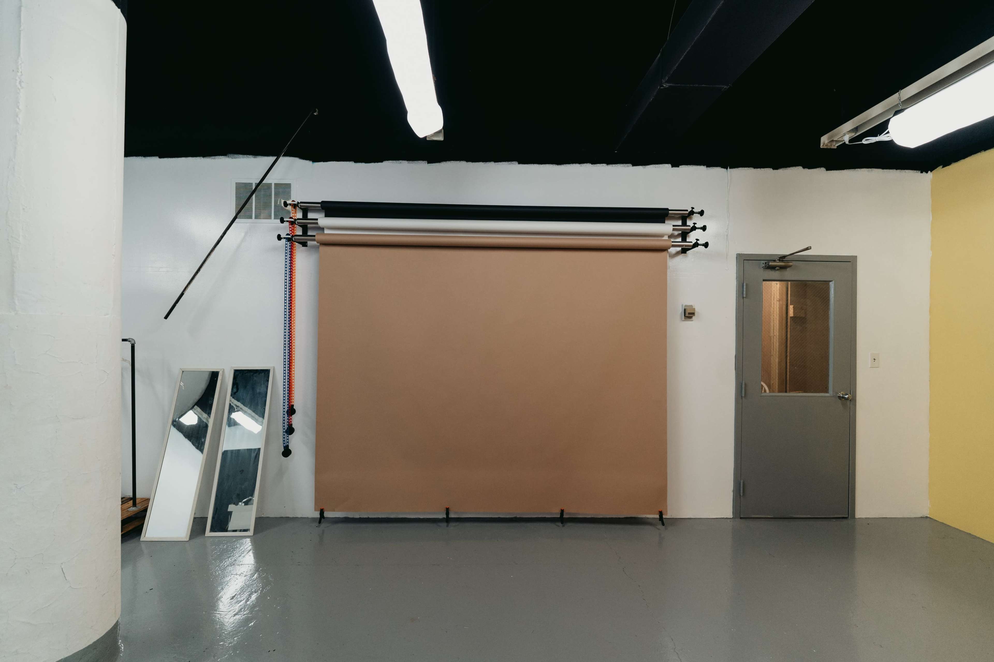 A photography studio with a brown backdrop, a mirror, and a door, set against a partially painted wall.