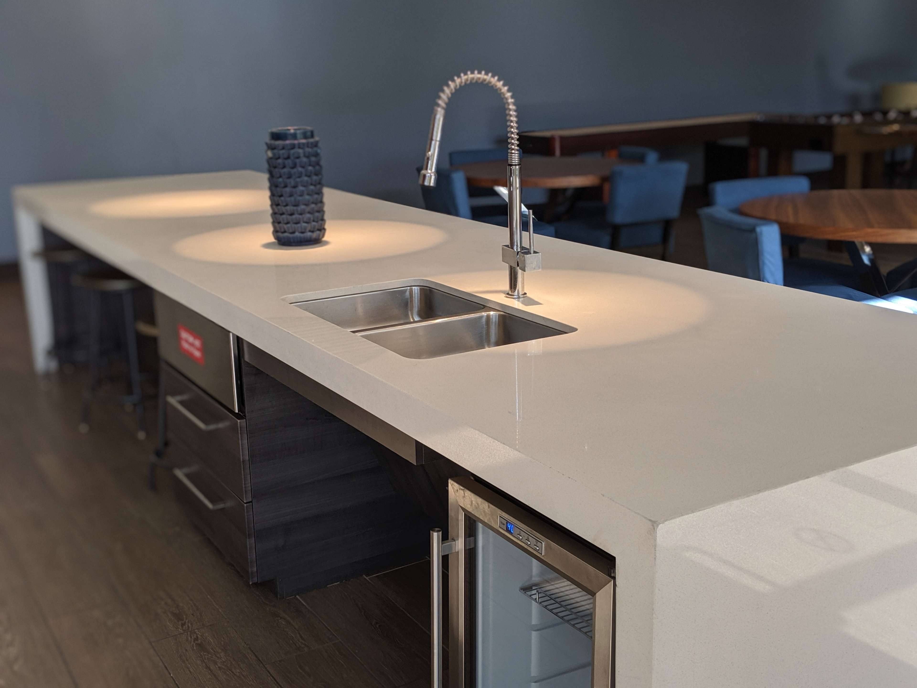 A modern kitchen countertop featuring a stainless steel sink, a faucet, and a small refrigerator, with ambient lighting highlighting the space.