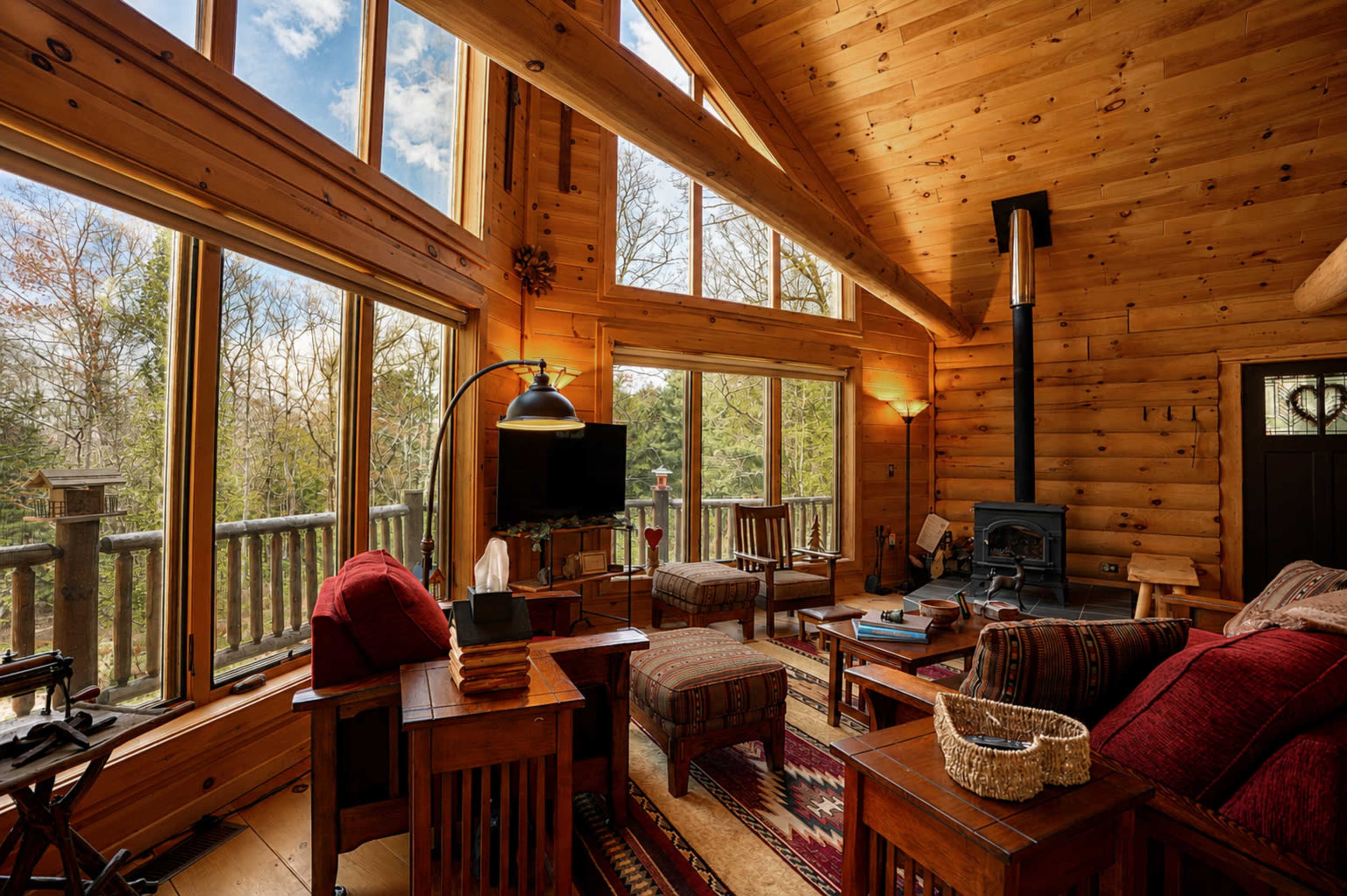 The image shows a wooden cabin living room with large windows, a fireplace, and rustic furniture.