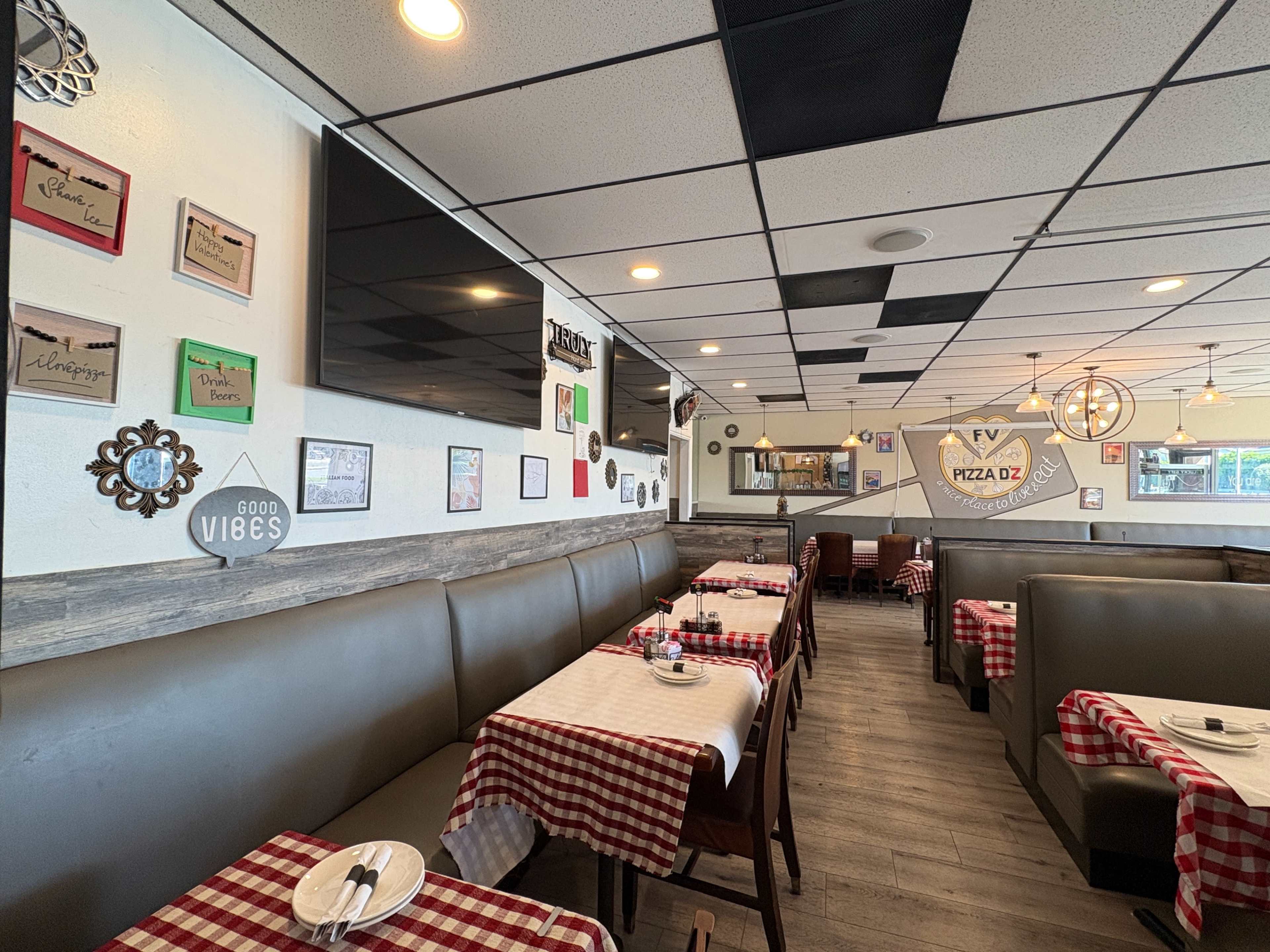 The interior of a restaurant features checkered tablecloths, wall decorations, and a large wall-mounted television.