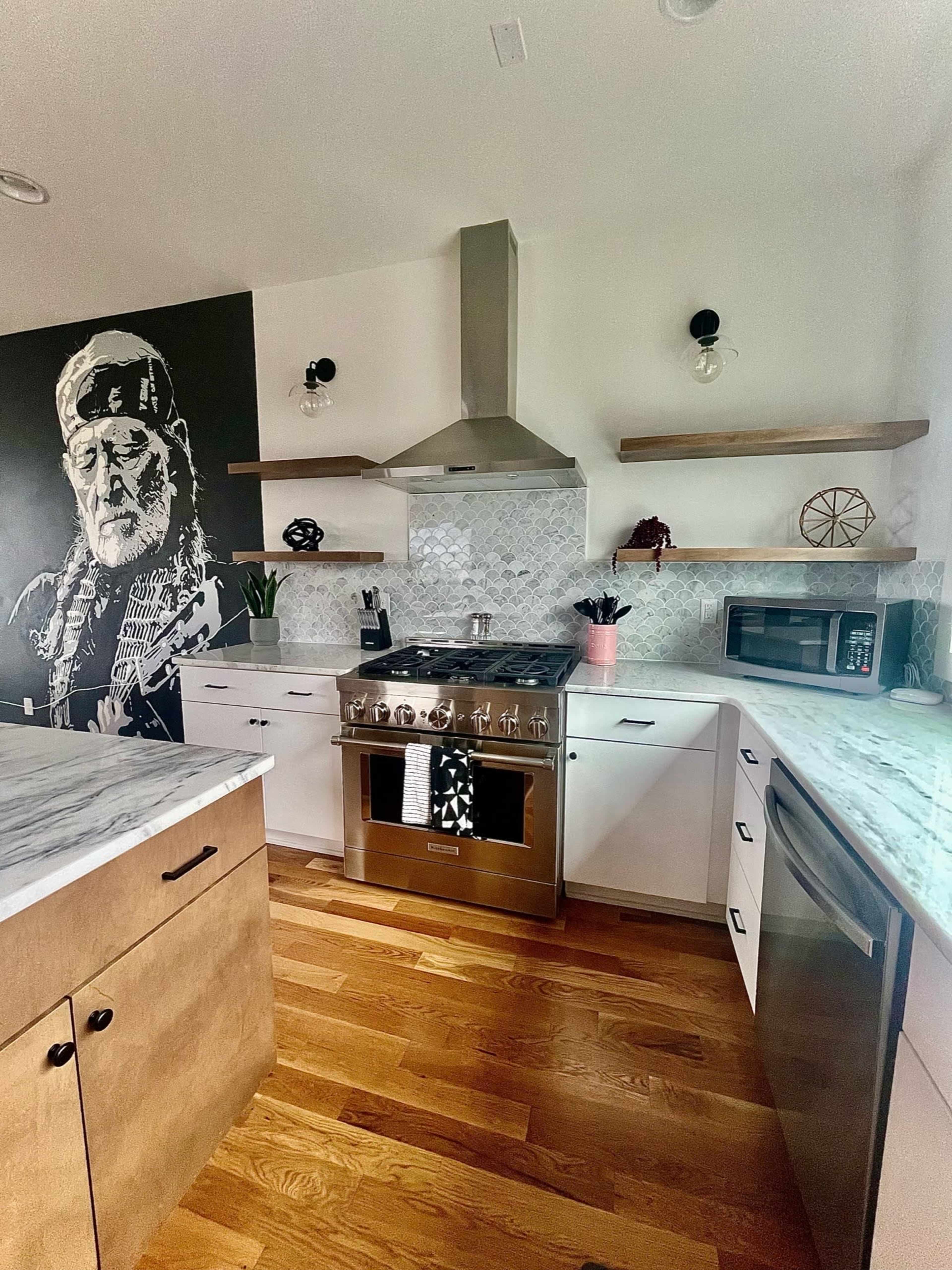 The kitchen features a modern design with a large stainless steel stove, marble countertops, and a mural of an elderly man on one wall.