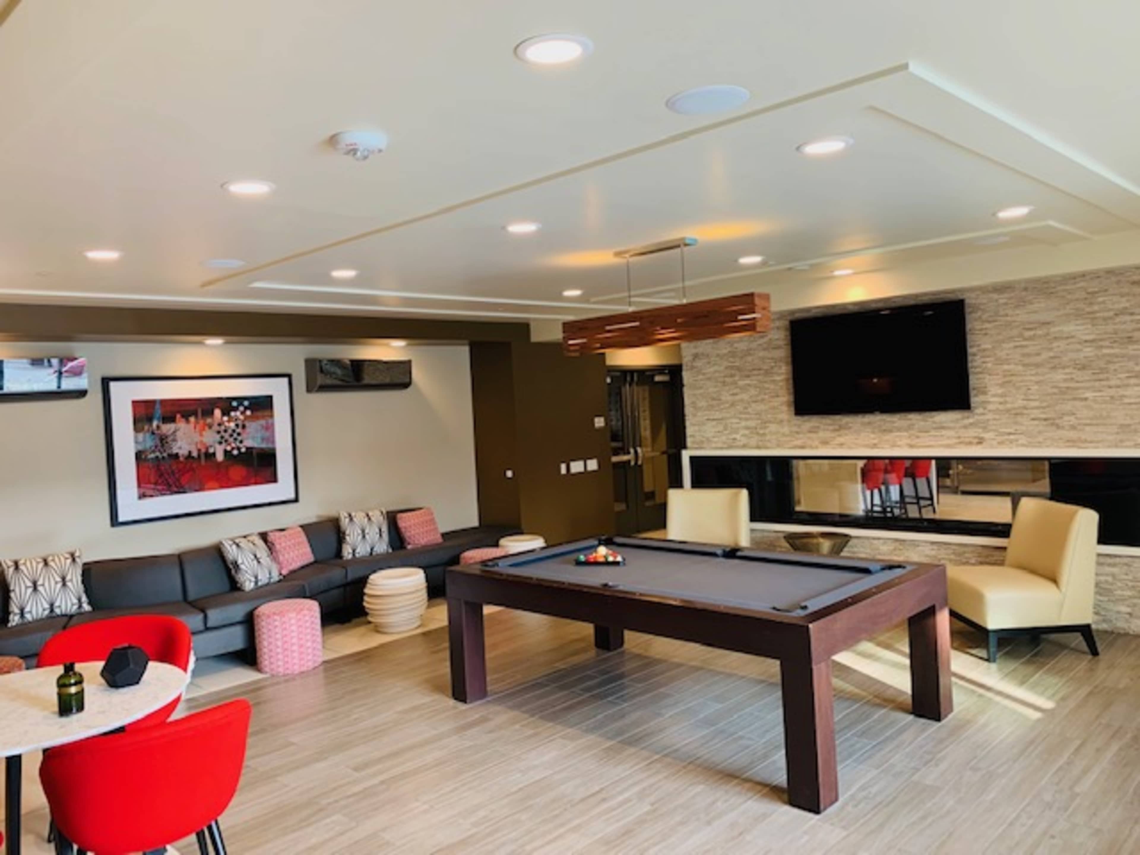 A modern recreational room featuring a pool table, a seating area with a sofa, and a table with chairs, all illuminated by recessed lighting.